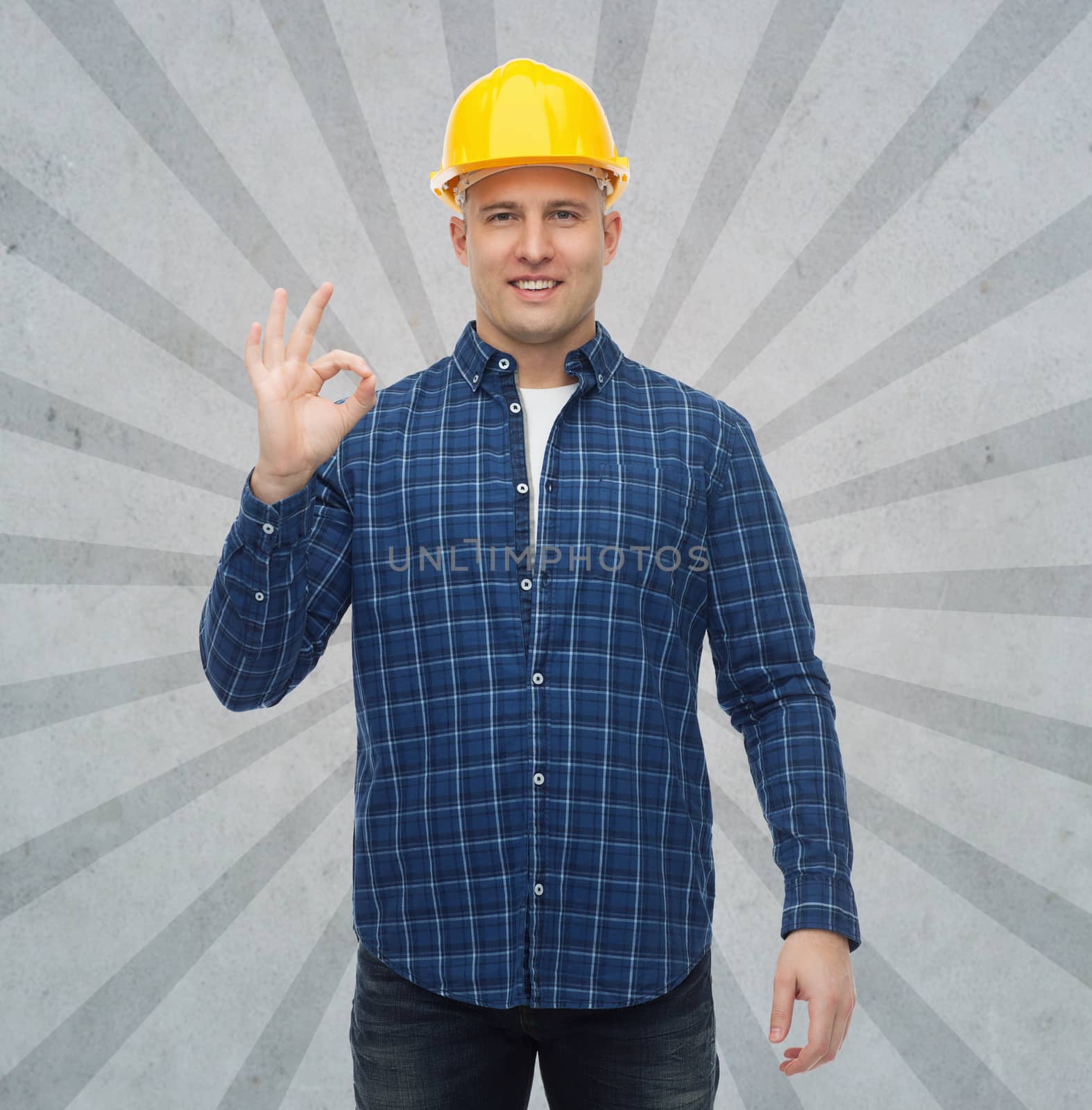 repair, construction, building, people and maintenance concept - smiling male builder or manual worker in helmet showing ok sign over gray burst rays background