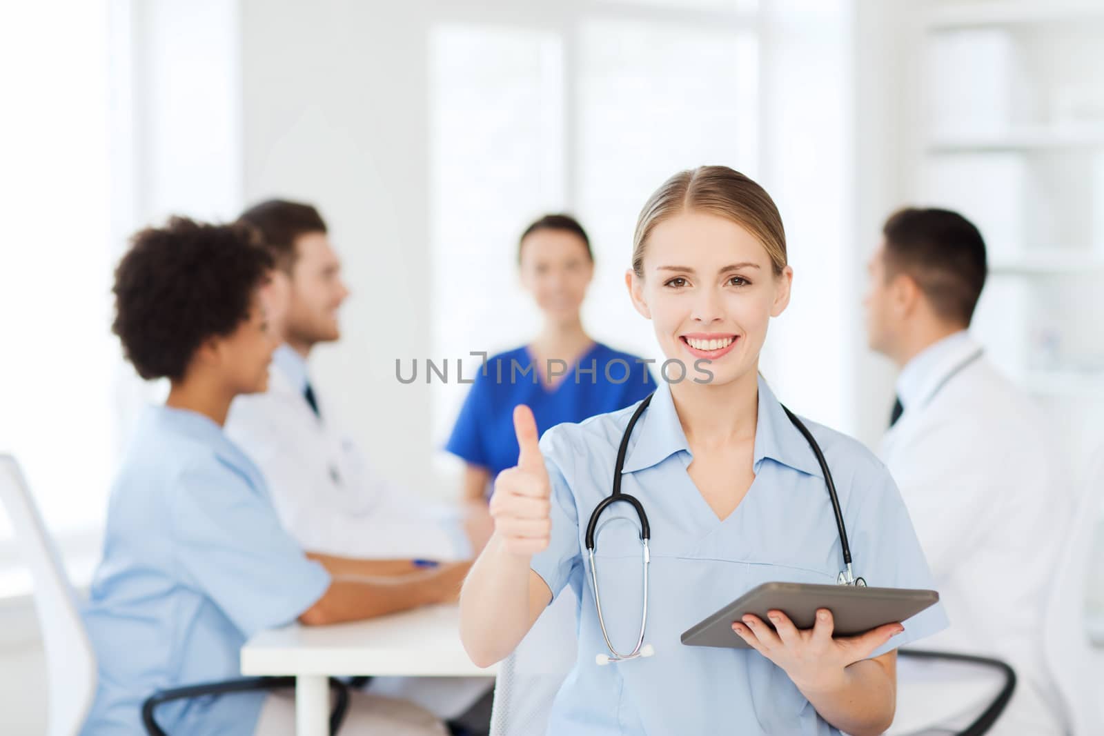 clinic, profession, people and medicine concept - happy female doctor with tablet pc computer over group of medics meeting at hospital showing thumbs up gesture