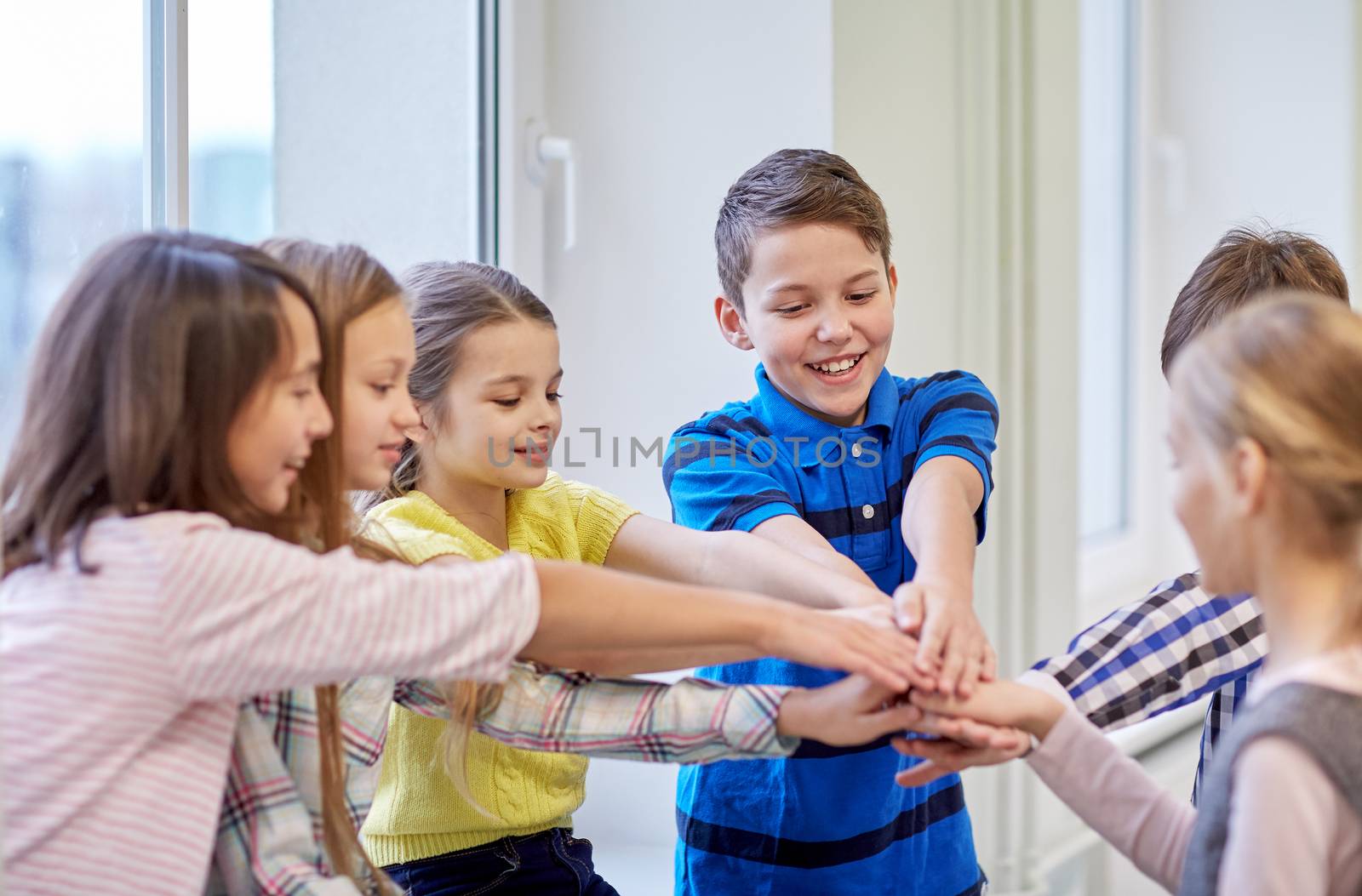 education, elementary school, children, break and people concept - group of smiling school kids putting hands on top in corridor