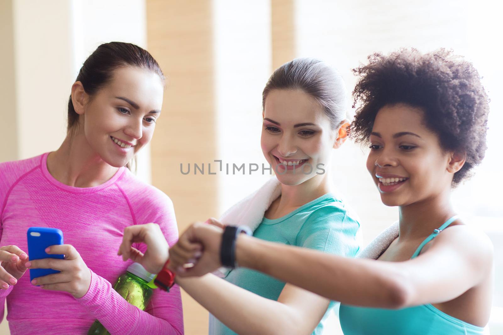 happy women showing time on wrist watch in gym by dolgachov