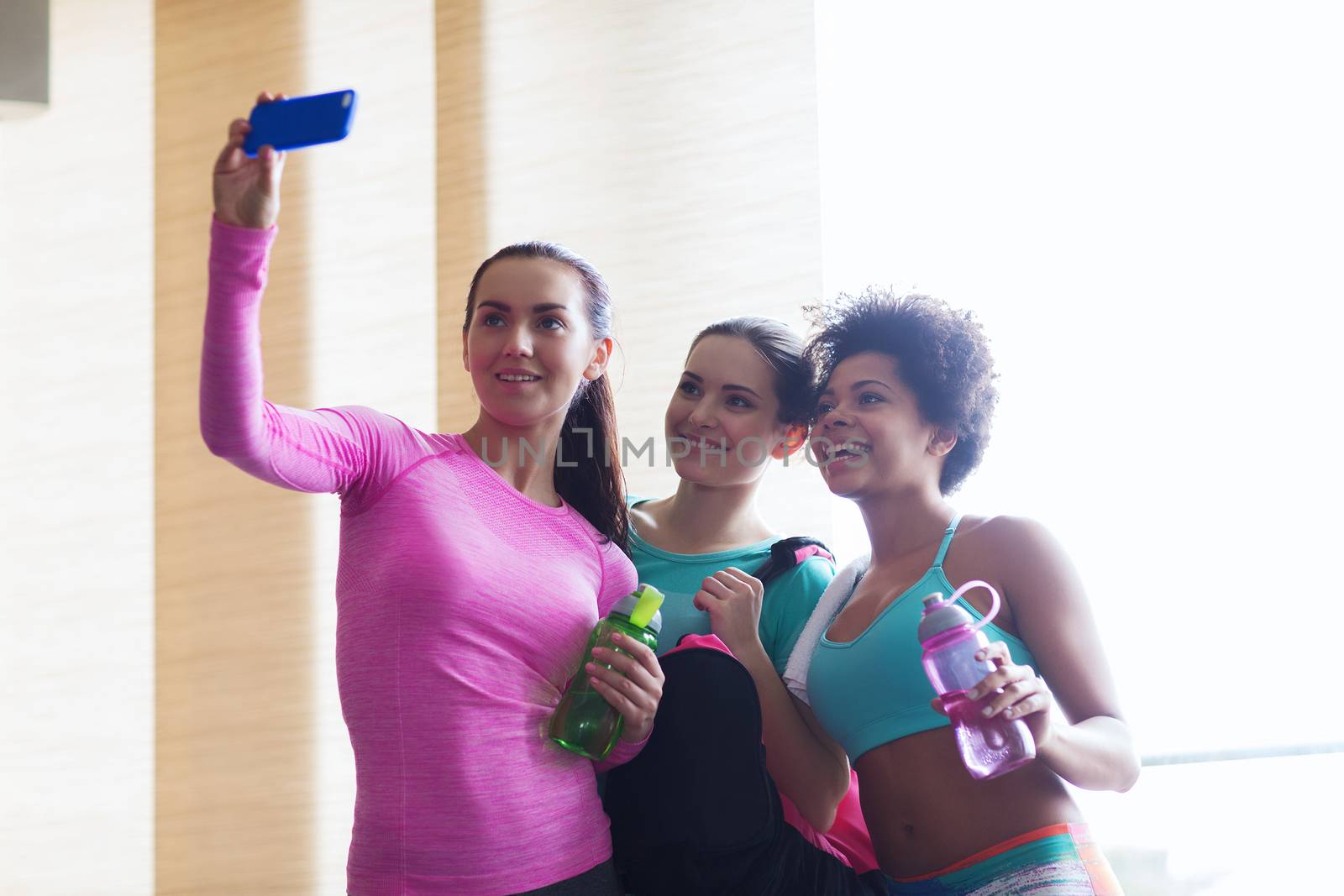 happy women with smartphone taking selfie in gym by dolgachov