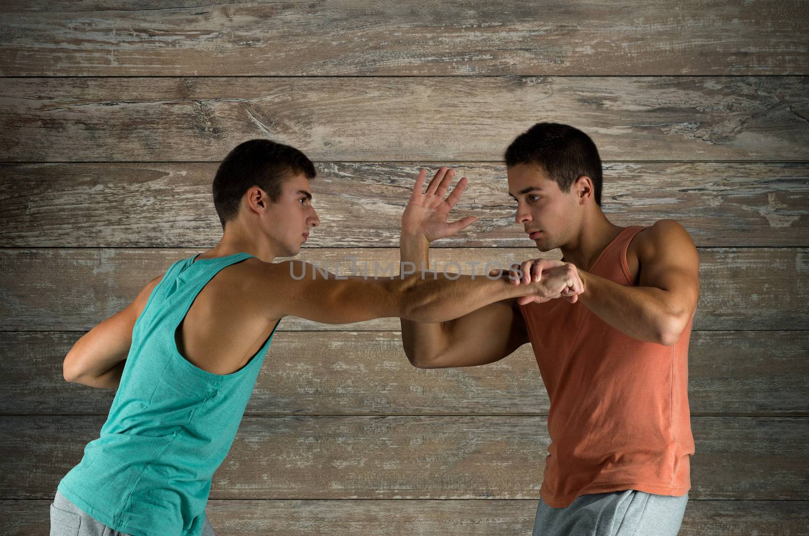 sport, competition, strength and people concept - young men fighting hand-to-hand over wooden wall background