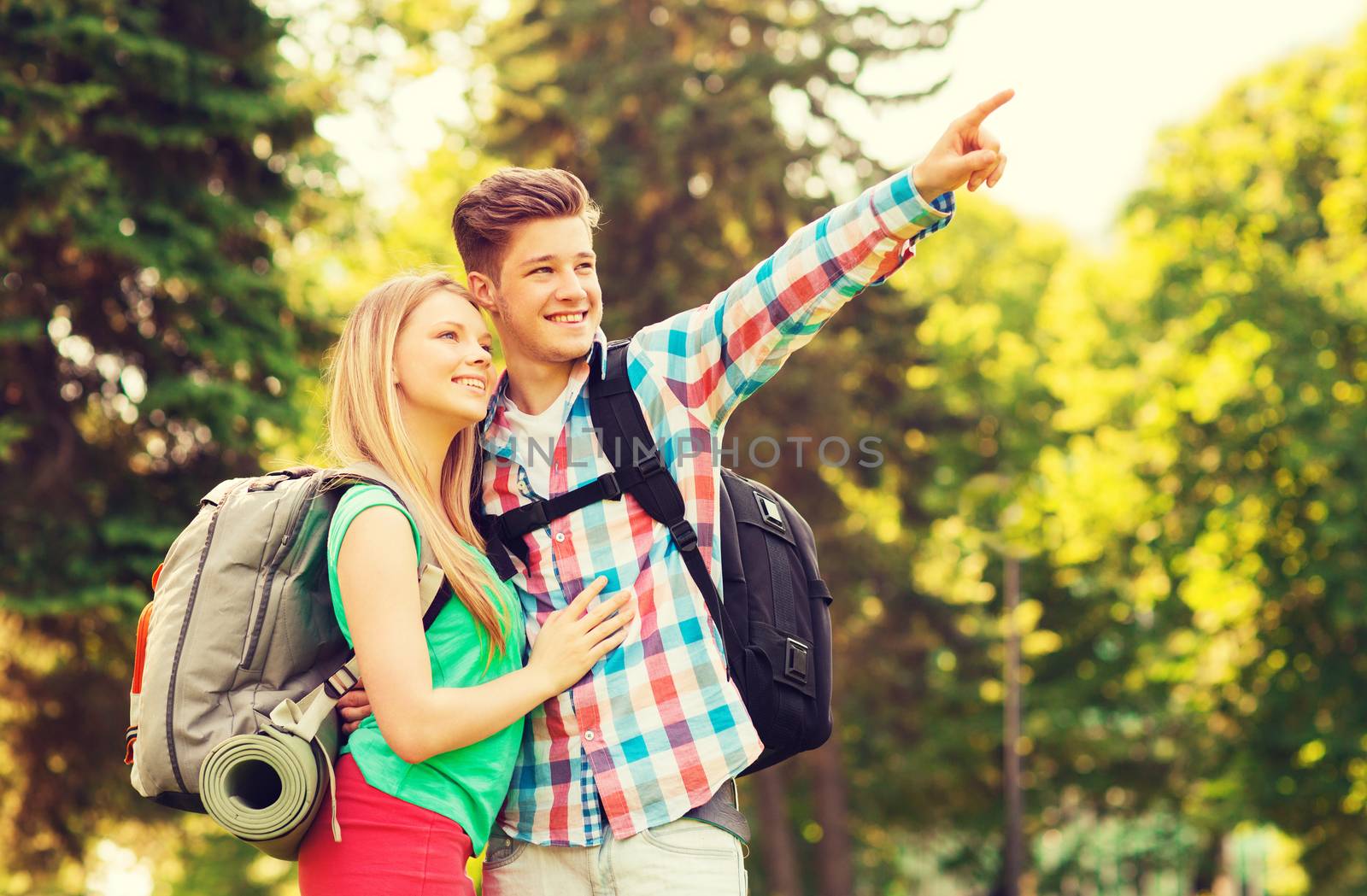 travel, vacation, tourism and friendship concept - smiling couple with backpacks pointing finger in nature