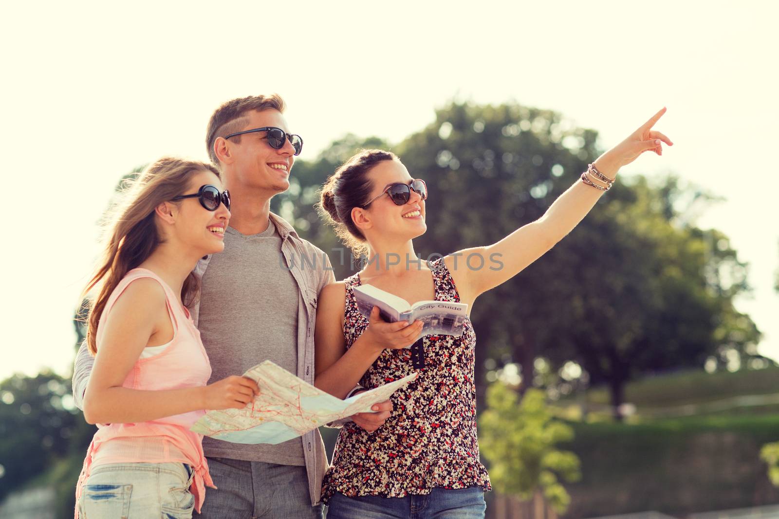 friendship, travel, tourism, vacation and people concept - smiling friends with map and city guide pointing finger outdoors