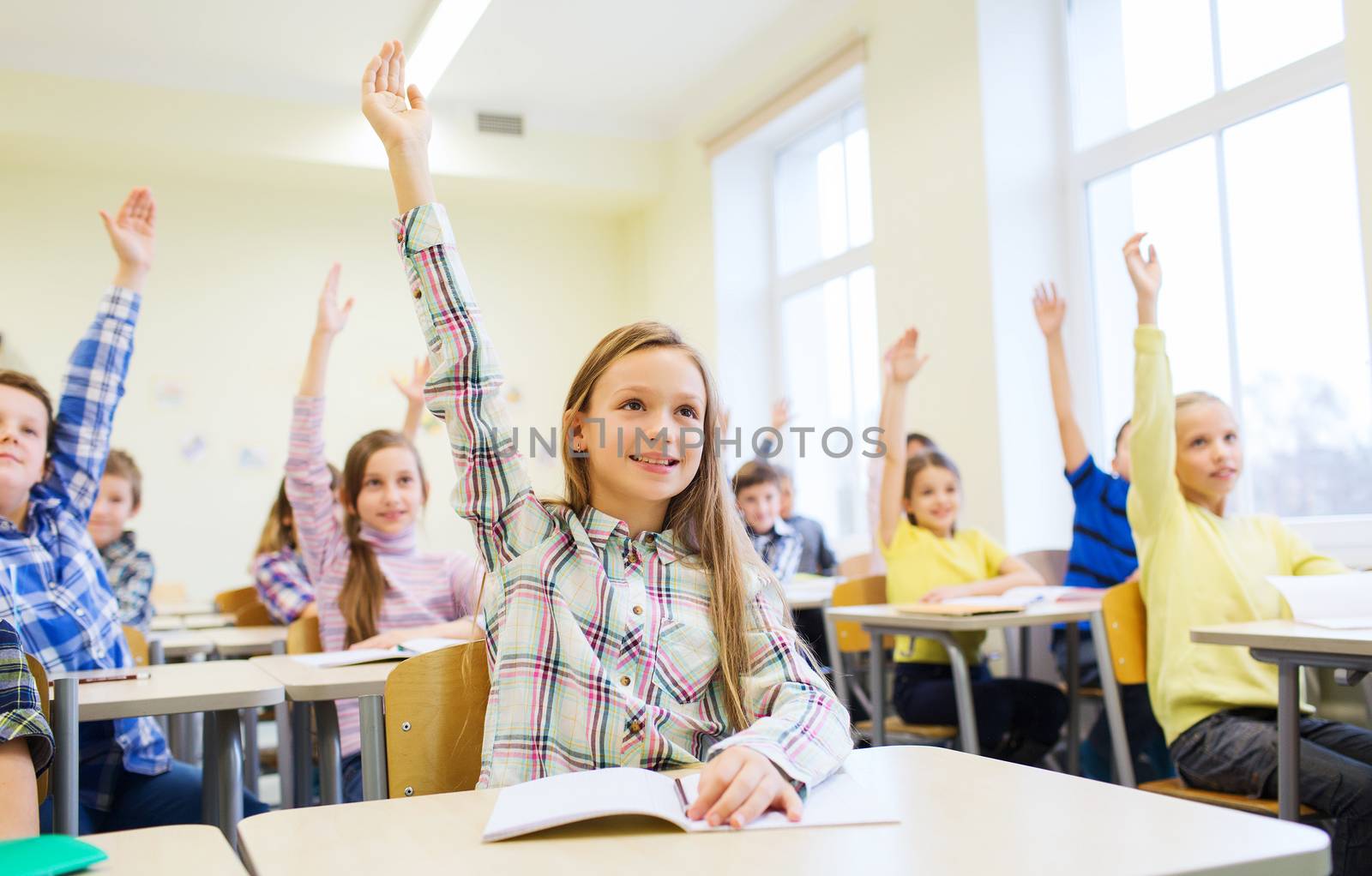 education, elementary school, learning and people concept - group of school kids with notebooks sitting in classroom and raising hands