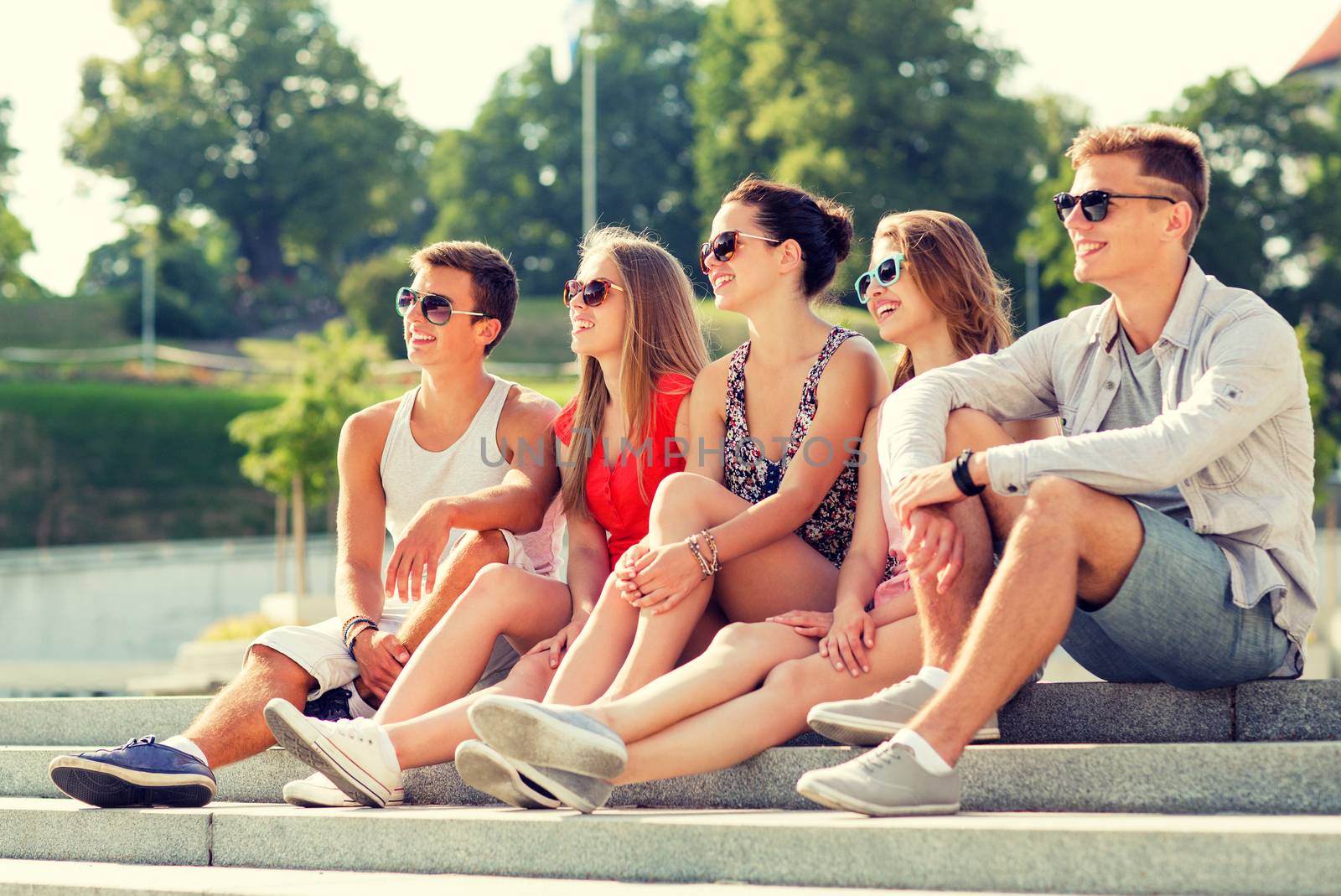 friendship, leisure, summer and people concept - group of smiling friends sitting on city square