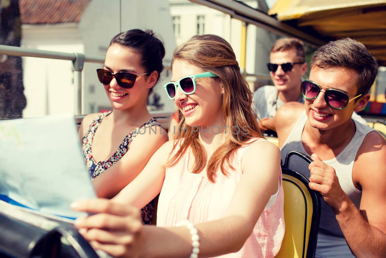 friendship, travel, vacation, summer and people concept - group of smiling friends with map traveling by tour bus