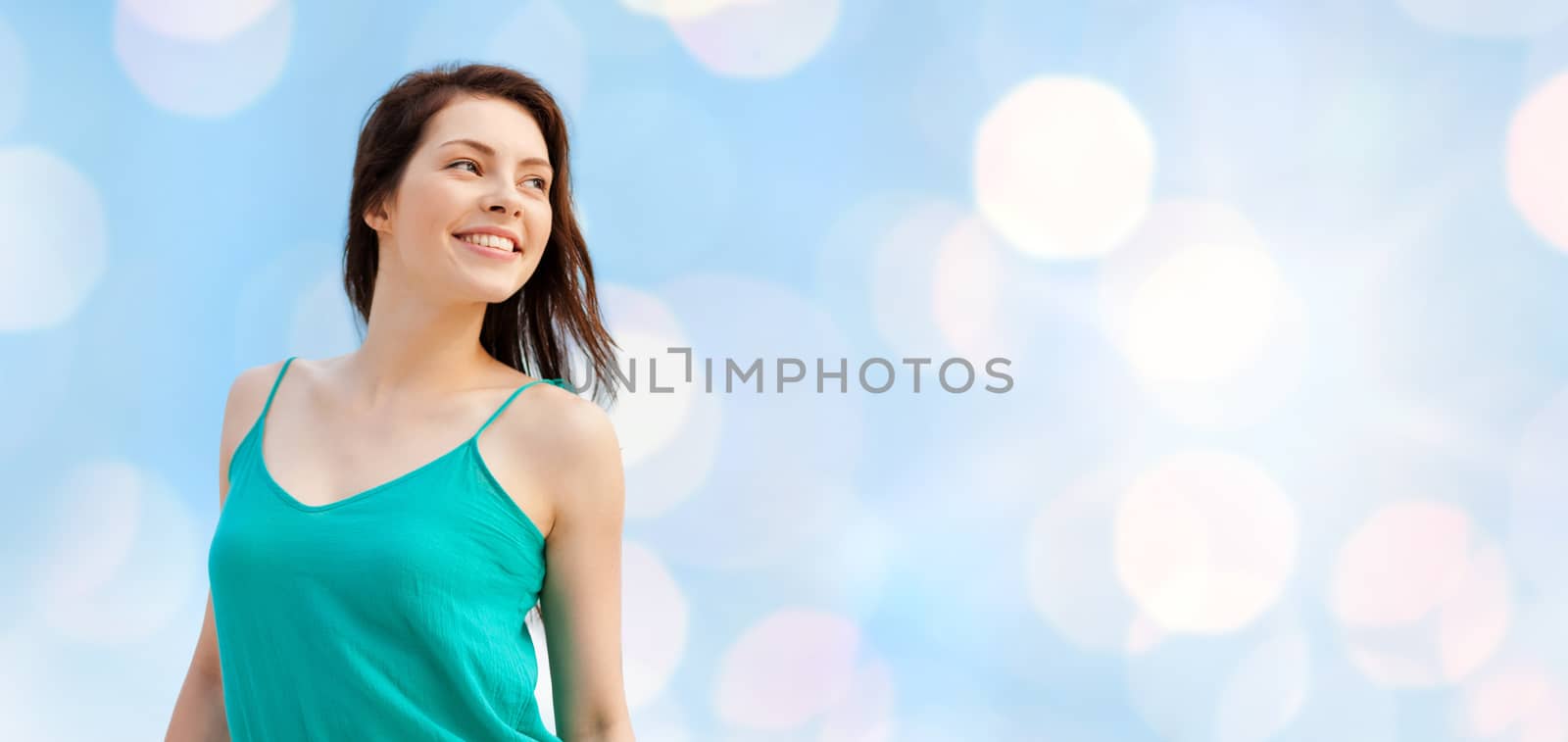 summer holidays, people, youth and happiness concept - happy girl or young woman looking aside over blue lights background