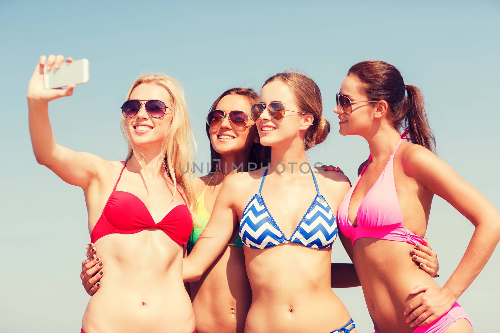 summer vacation, holidays, travel, technology and people concept- group of smiling young women on beach making selfie with smartphone over blue sky background