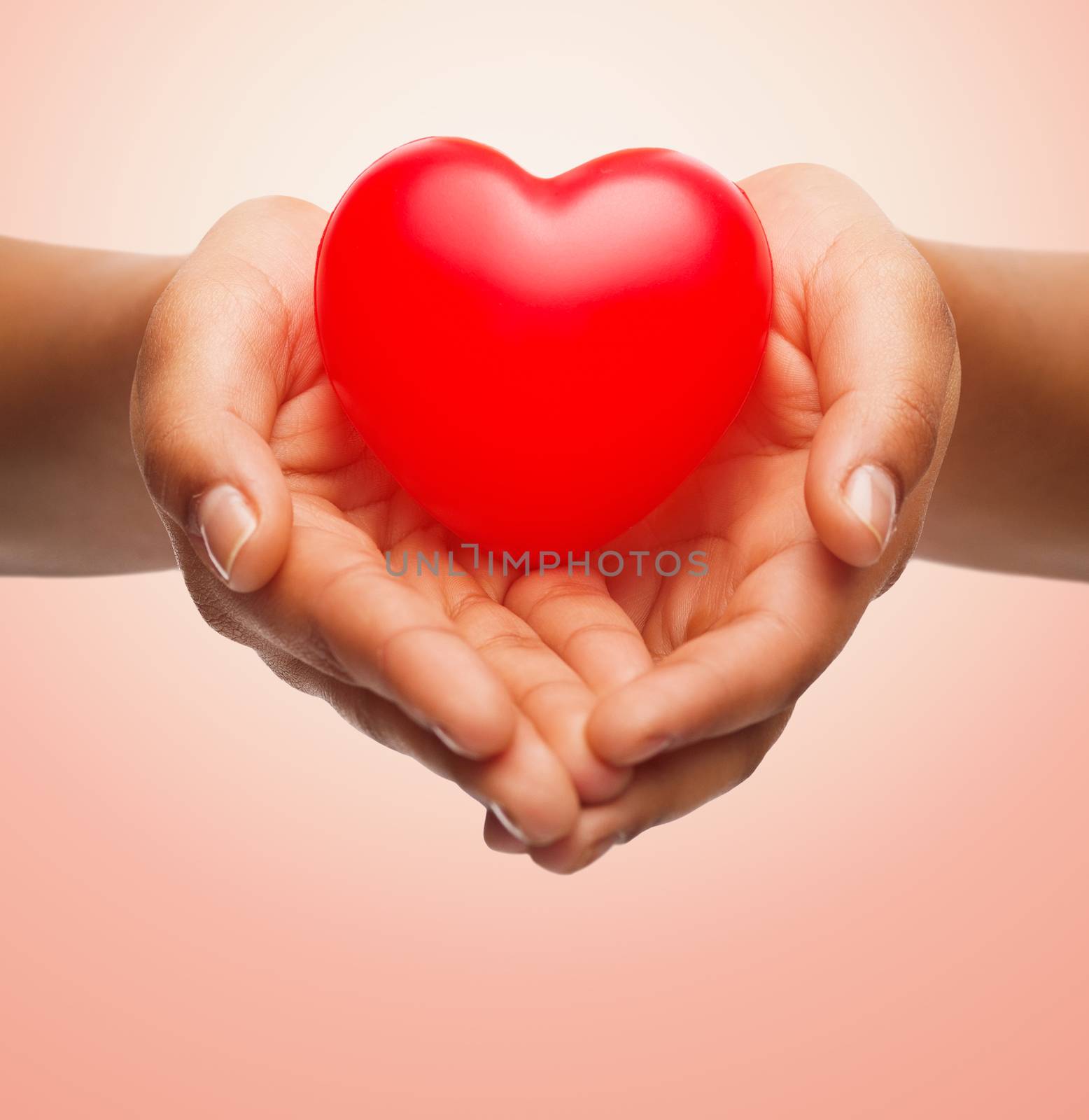 health, medicine, love, valentines day and charity concept - close up of african american female hands holding small red heart over beige background