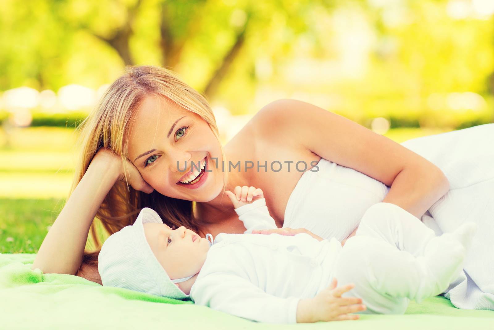 family, child and parenthood concept - laughing mother lying with little baby on blanket in park