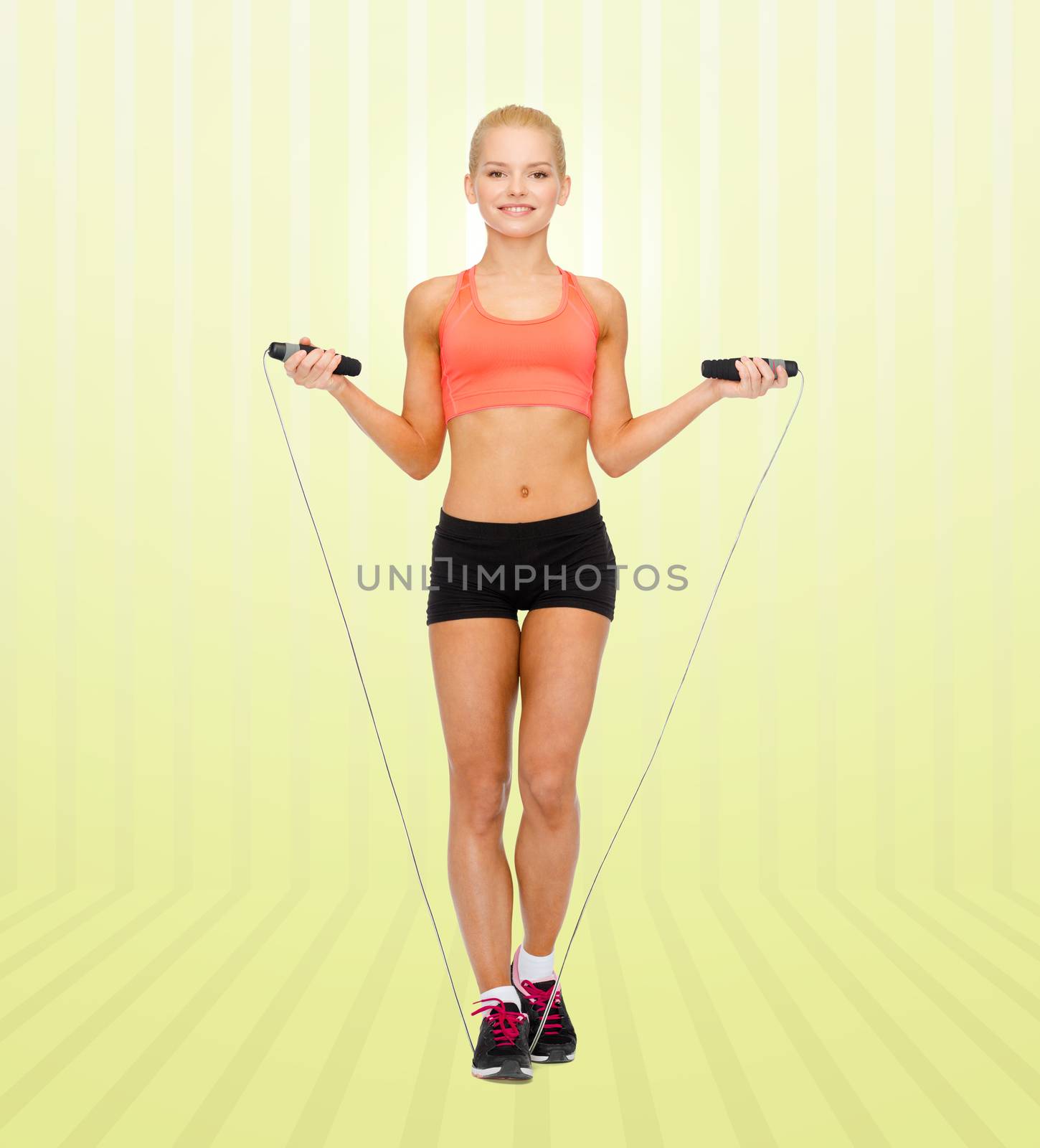 sport, fitness, people and weight loss - smiling sporty woman jumping with skipping rope over yellow striped background