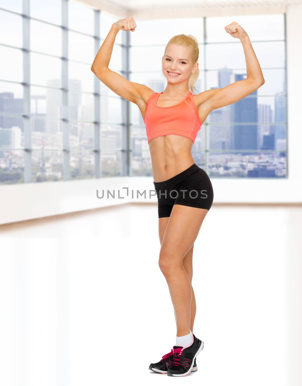 fitness, sport and people concept - smiling sporty woman showing her biceps over gym background