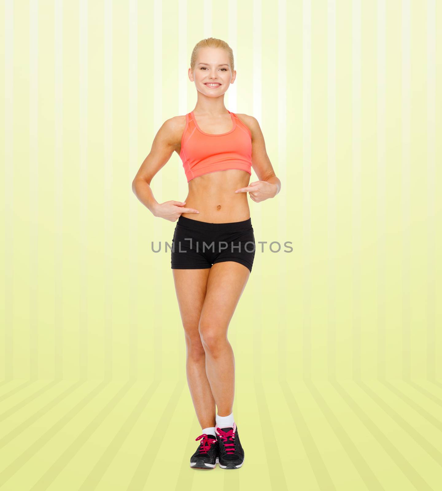 smiling sporty woman pointing at her six pack by dolgachov