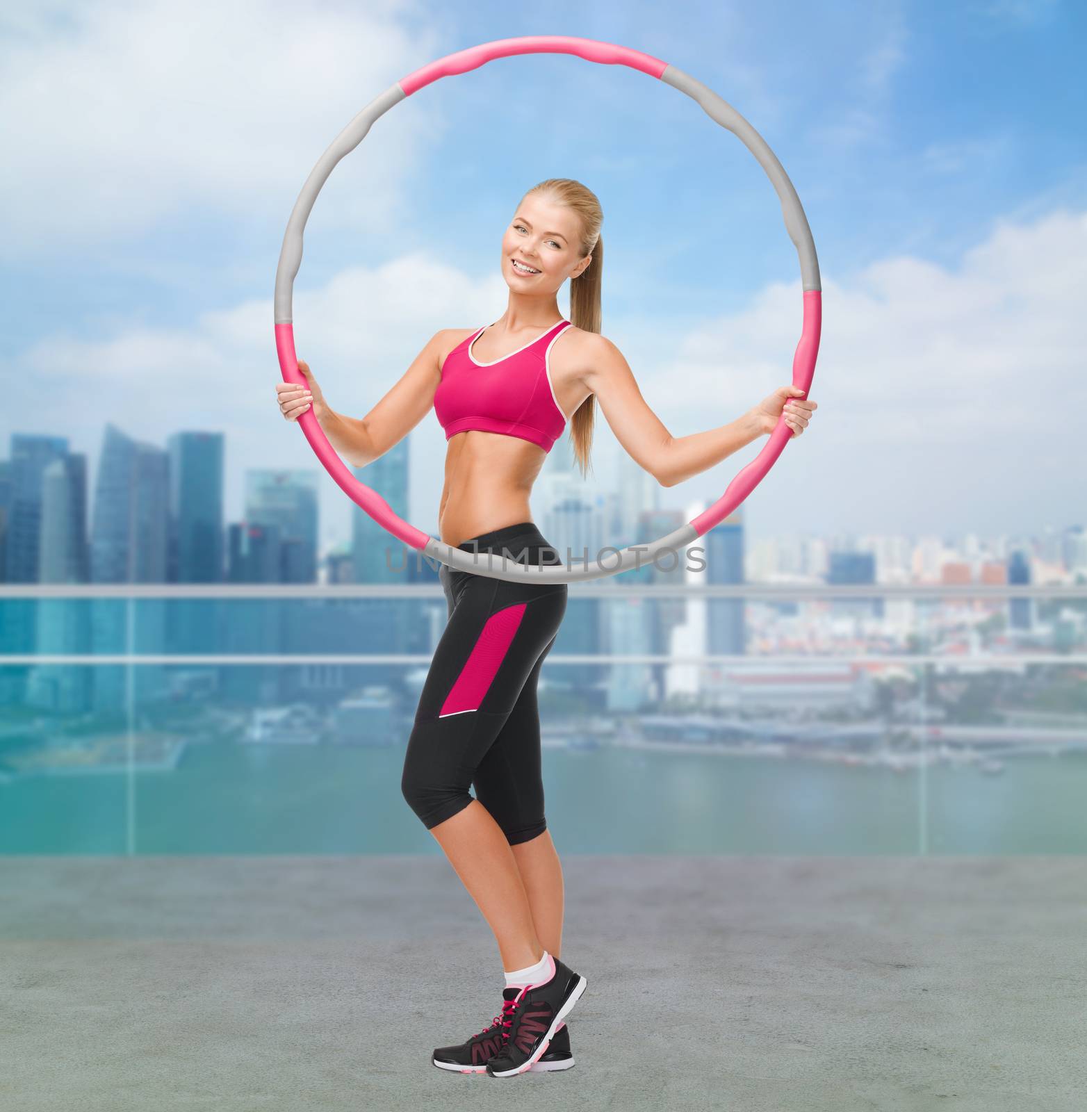 fitness, sport, people and healthcare concept - young sporty woman exercising with hula hoop over city waterside background