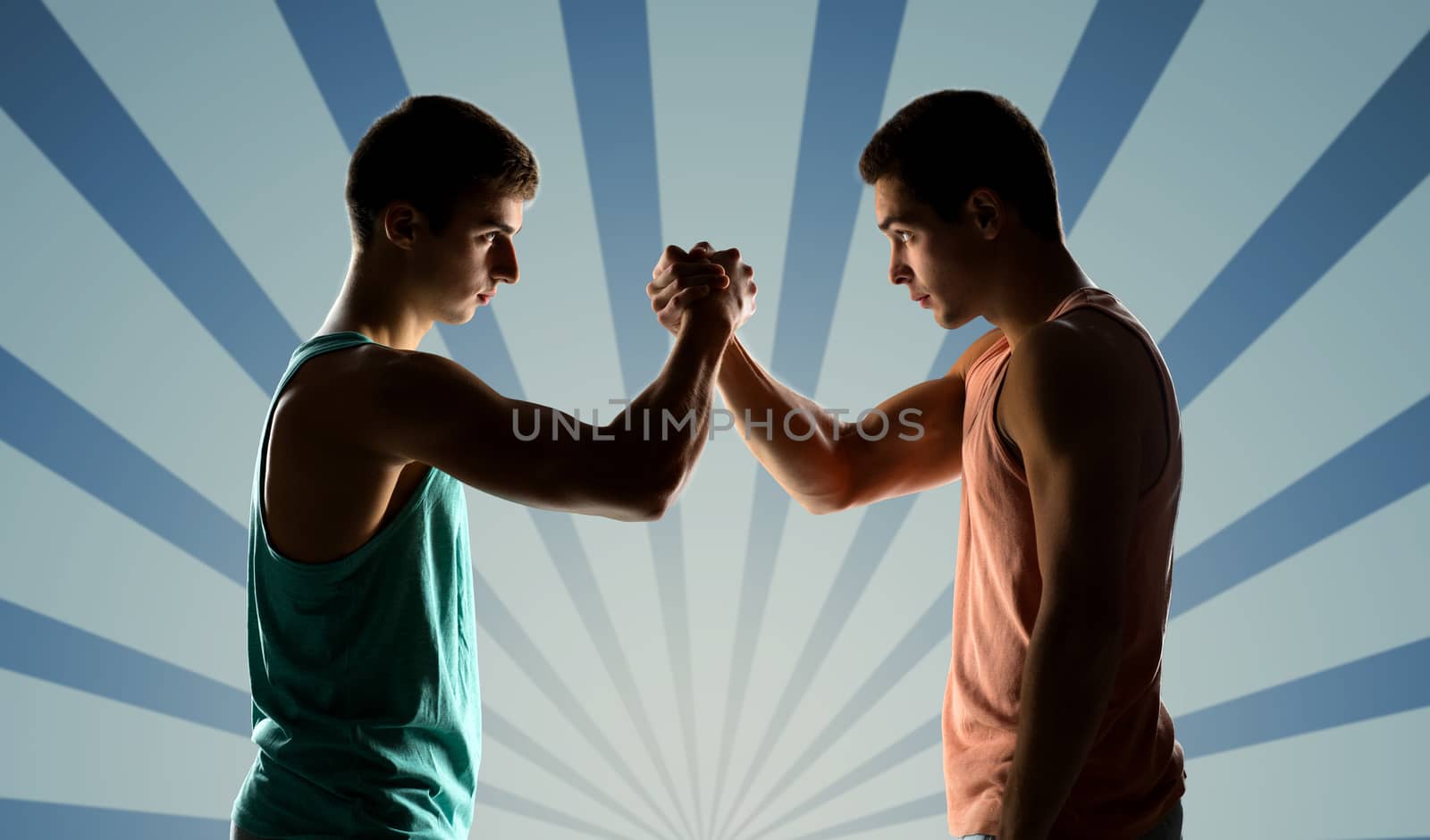 sport, competition, strength and people concept - two young men arm wrestling over blue burst rays background
