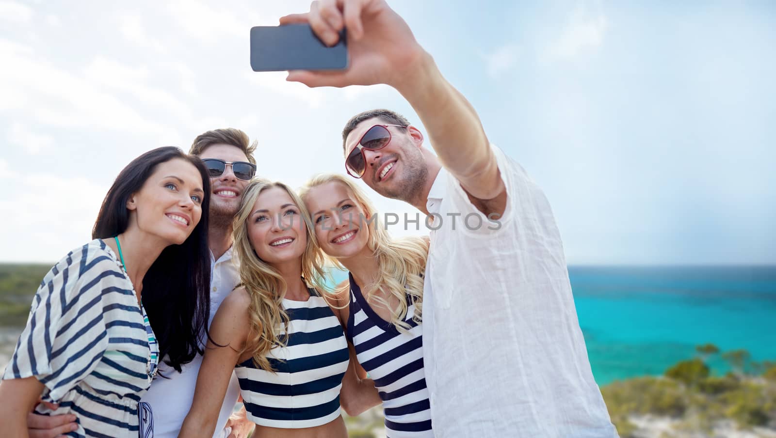 summer, sea, tourism, technology and people concept - group of smiling friends with smartphone photographing and taking selfie on beach