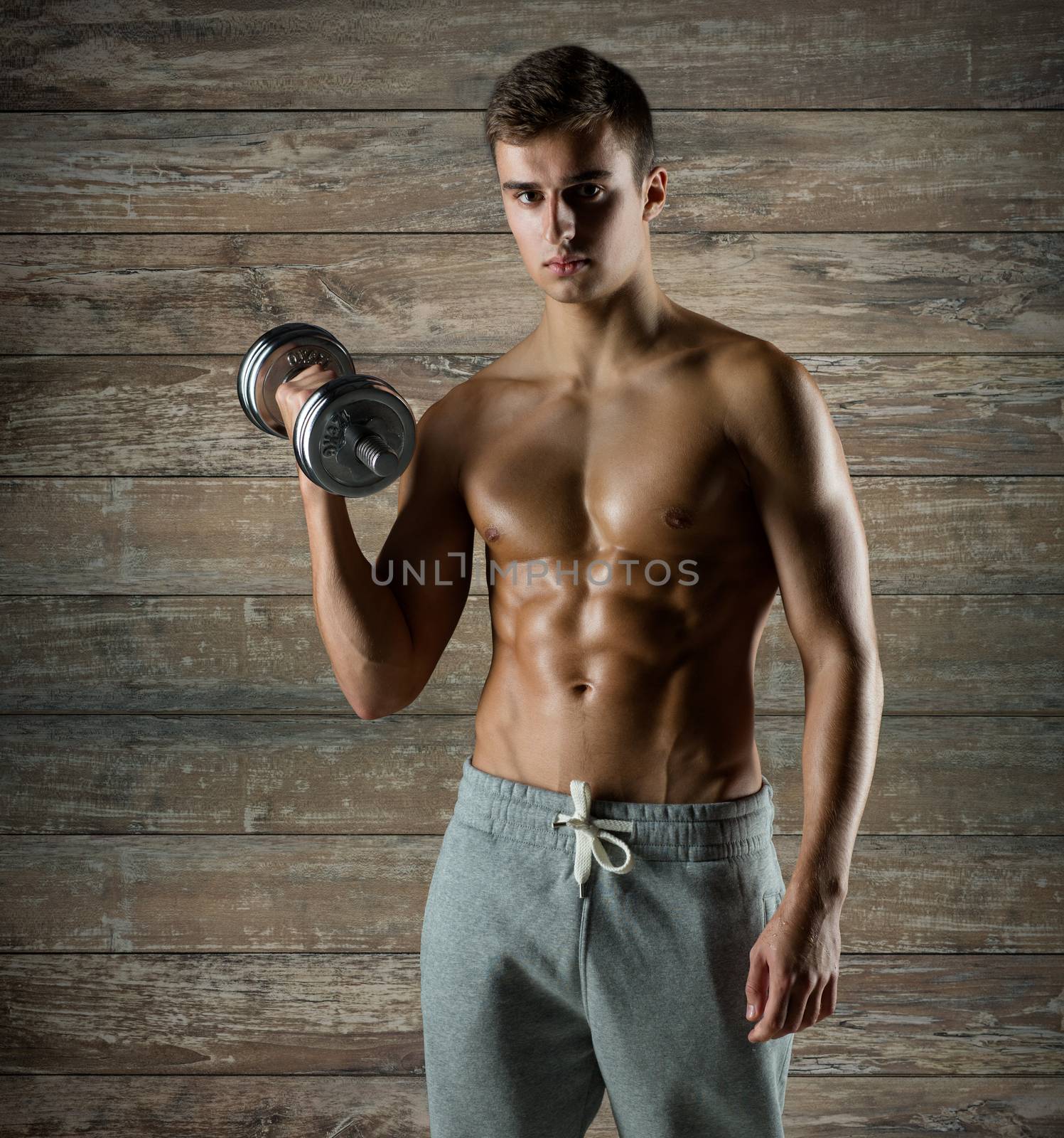 sport, fitness, weightlifting, bodybuilding and people concept - young man with dumbbell flexing biceps over wooden wall background