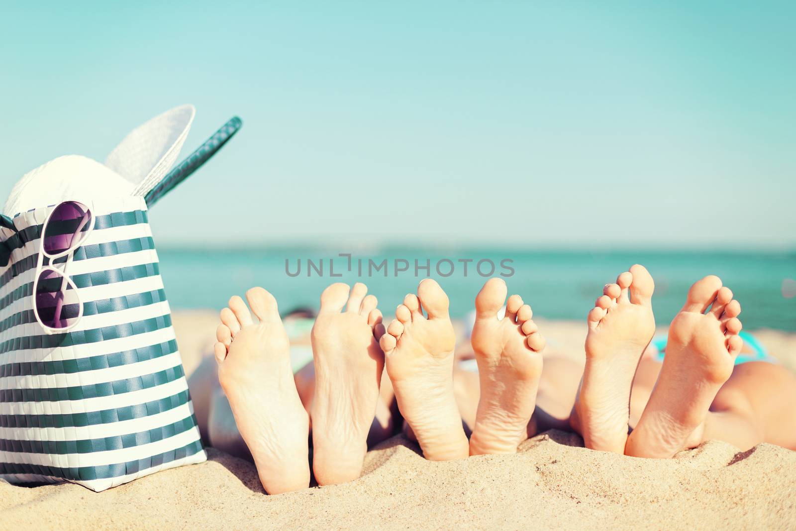 summer vacation, sunbathing and pedicure concept - three women lying on the beach with straw hat, sunglasses and bag