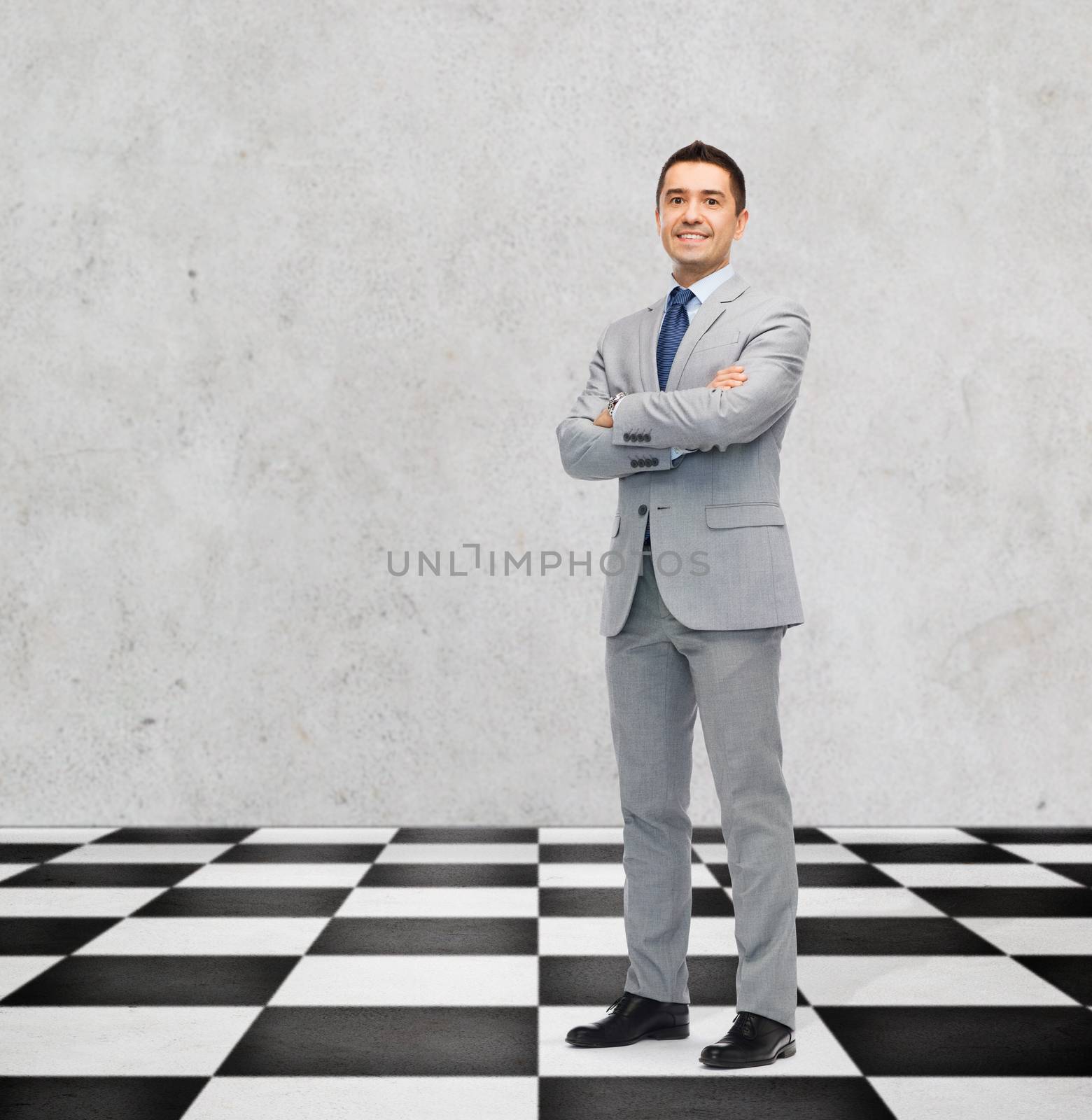 business, people and strategy concept - happy smiling businessman in suit standing on checkerboard pattern floor over gray background