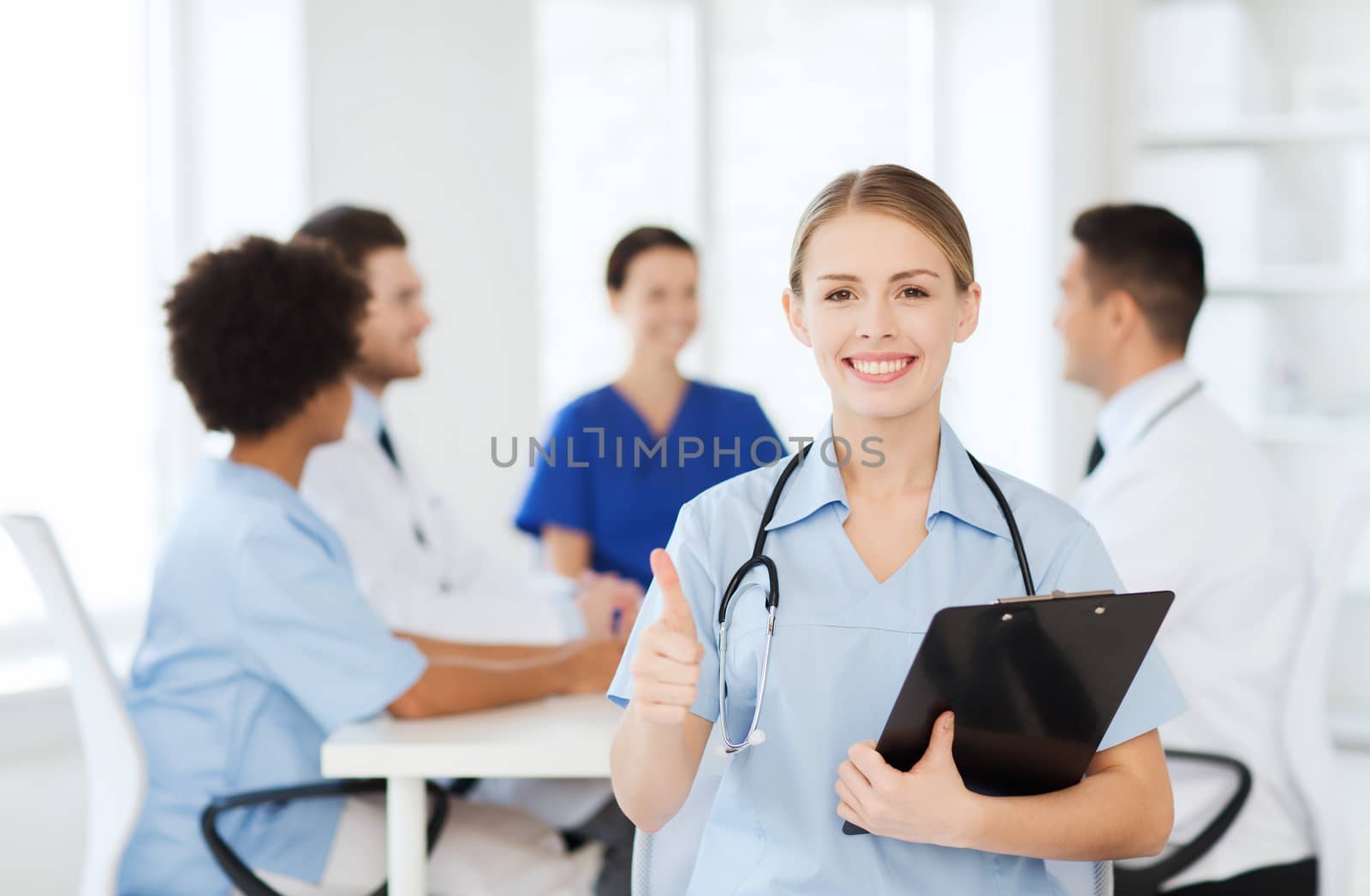 clinic, profession, people and medicine concept - happy female doctor with clipboard over group of medics meeting at hospital