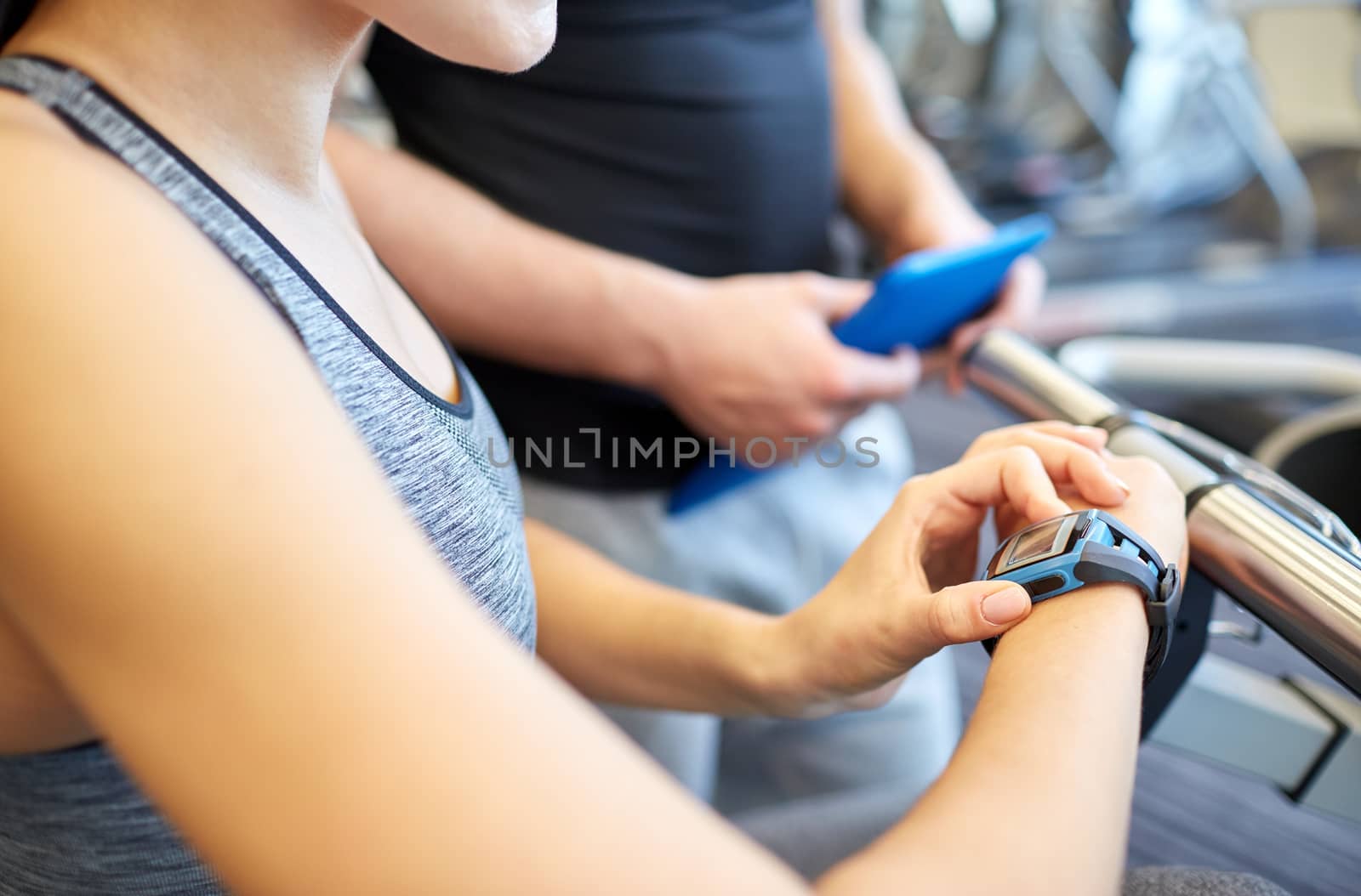 sport, fitness, lifestyle, technology and people concept - close up of woman setting heart-rate watch at gym with trainer