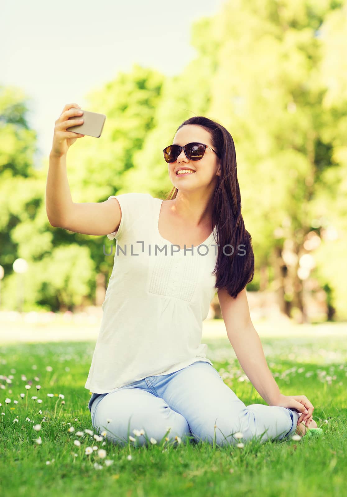 smiling young girl with smartphone sitting in park by dolgachov