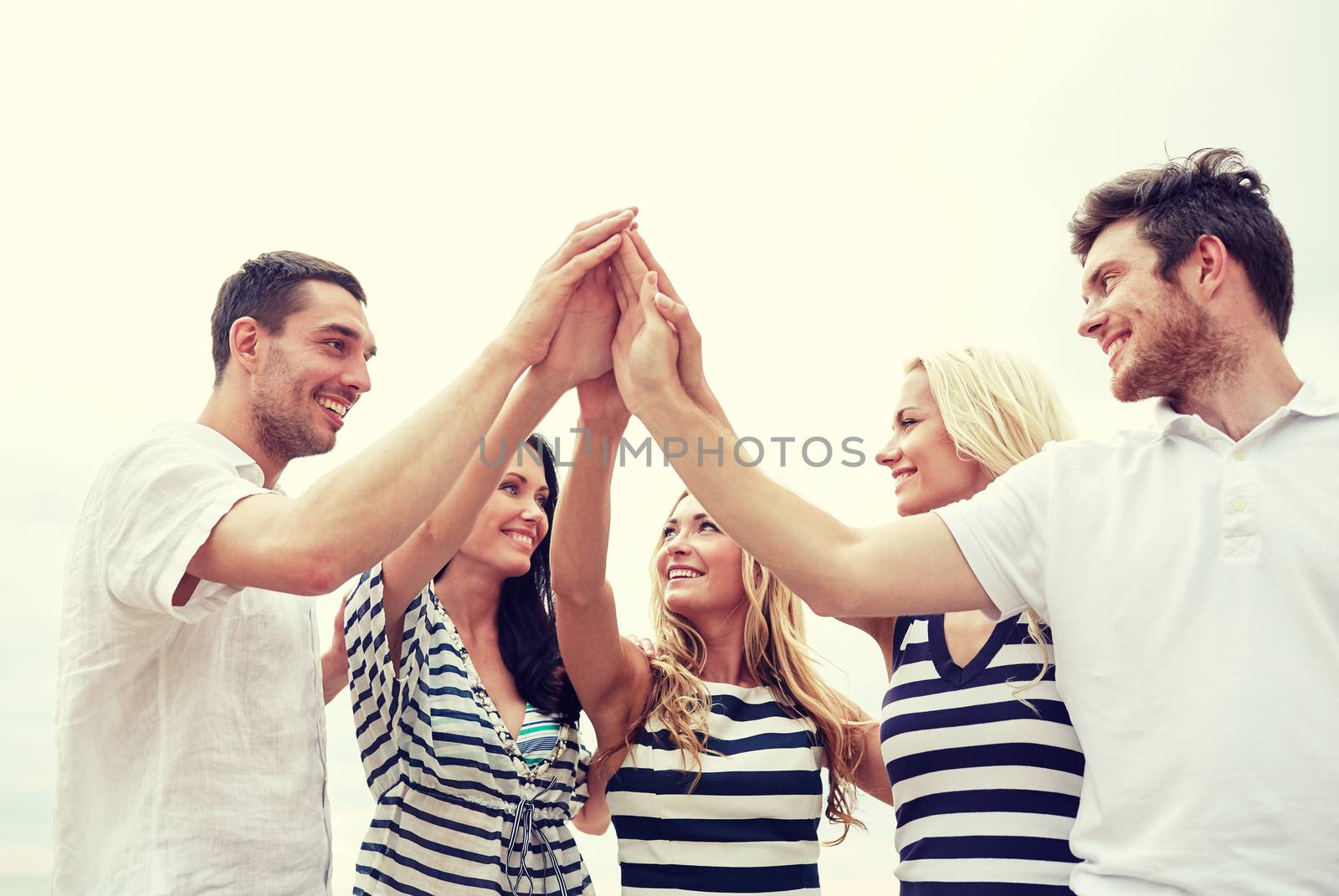 friendship, happiness, unity and people concept - smiling friends in striped clothes making high five gesture outdoors