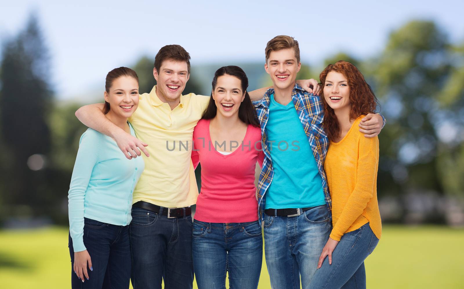friendship, summer vacation, nature and people concept - group of smiling teenagers standing and embracing over green park background