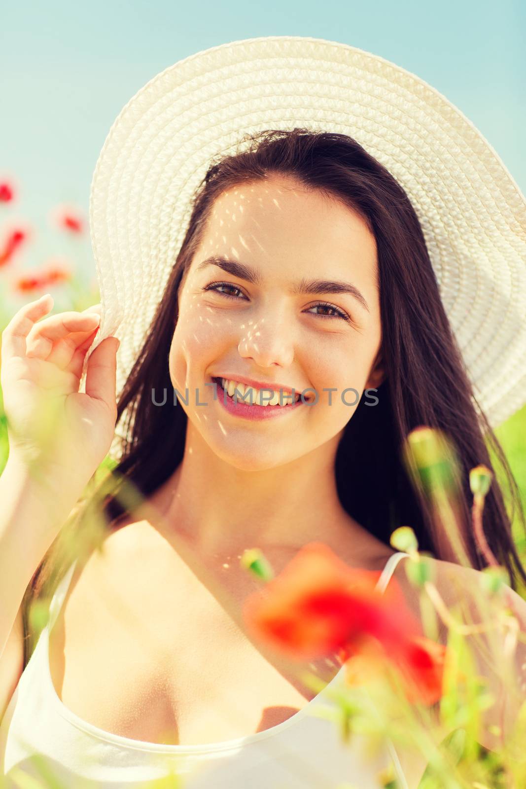 happiness, nature, summer, vacation and people concept - smiling young woman wearing straw hat on poppy field