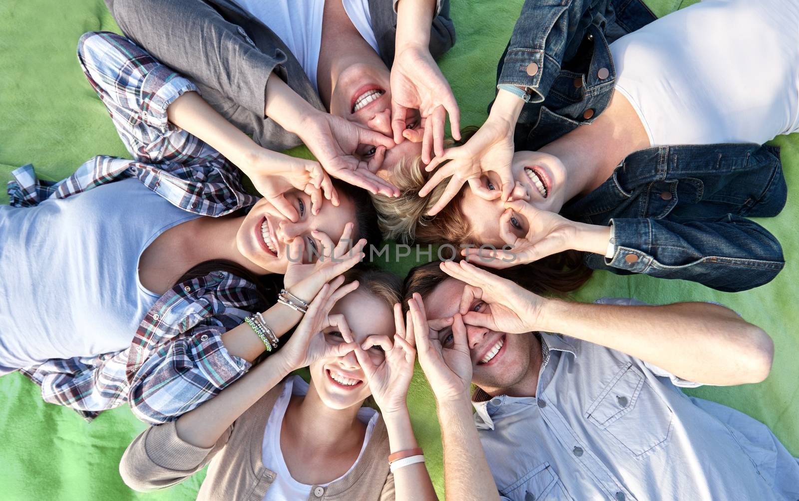 summer holidays, friendship, leisure and teenage concept - group of students or teenagers lying in circle and having fun at campus or park