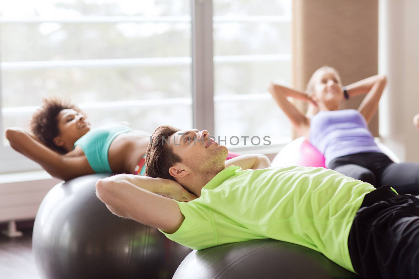 fitness, sport, training and lifestyle concept - group of people flexing abdominal muscles on fitball in gym