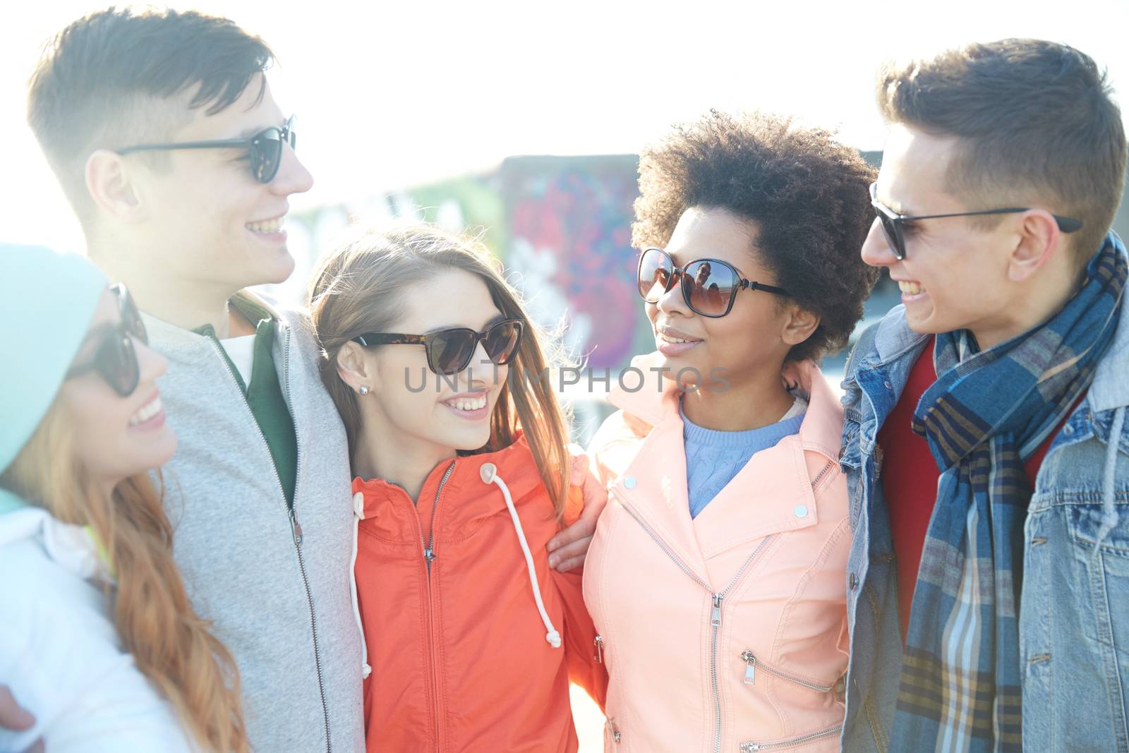 happy teenage friends in shades talking on street by dolgachov