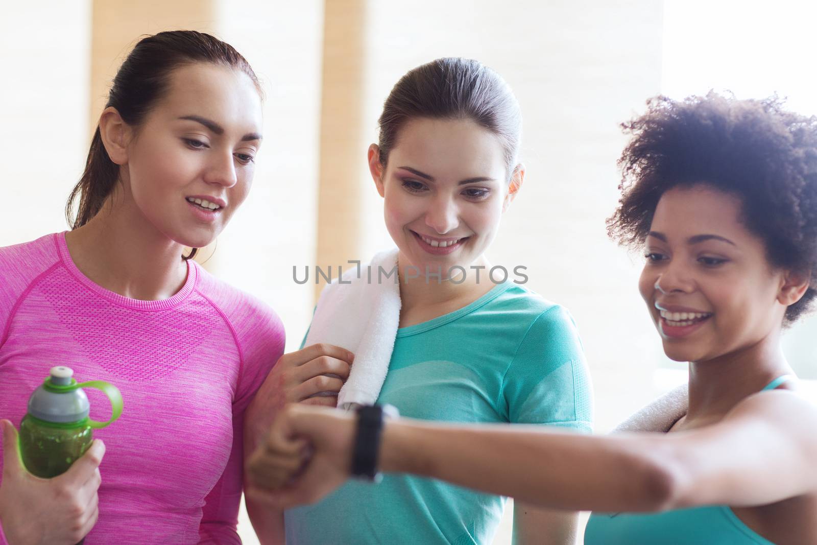 happy women showing time on wrist watch in gym by dolgachov