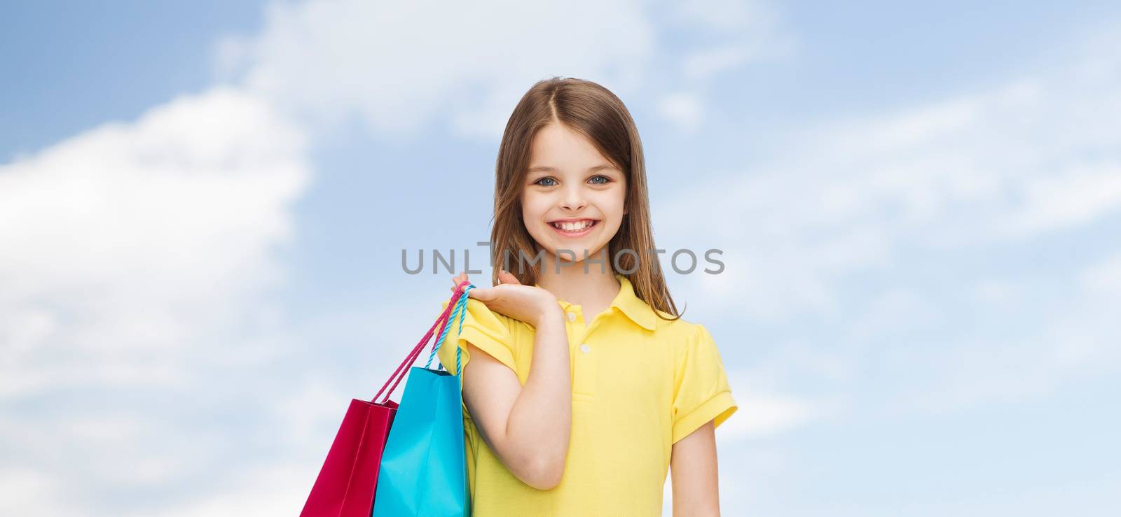 shopping, happiness and people concept - smiling little girl in yellow dress with shopping bags