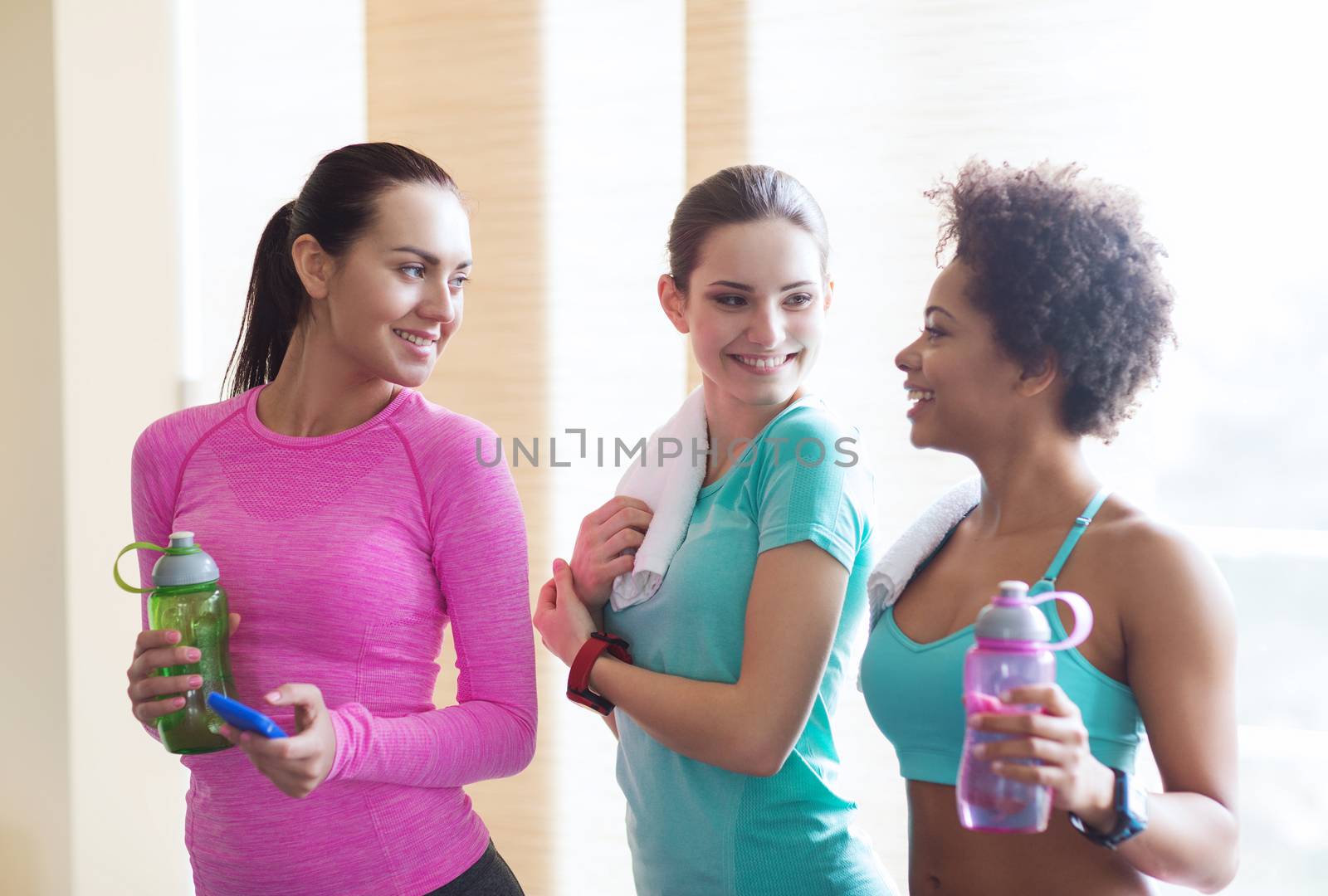 happy women with bottles of water in gym by dolgachov