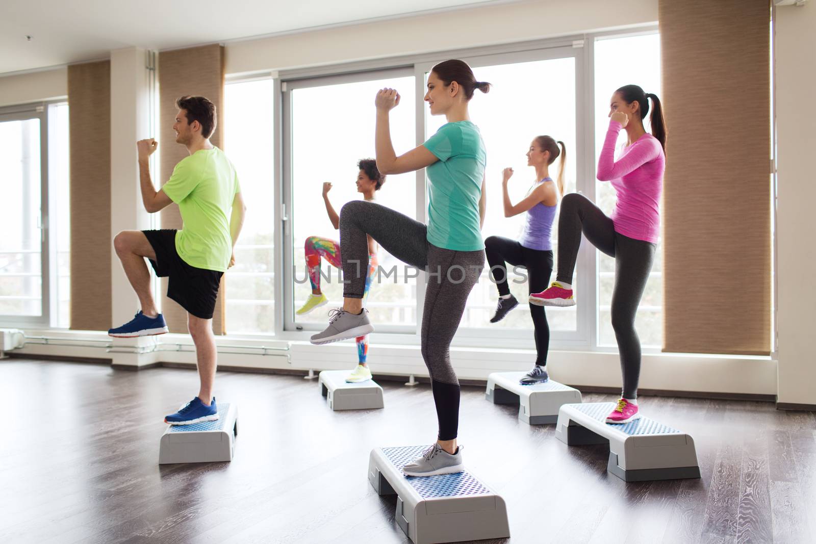 fitness, sport, training, aerobics and people concept - group of people working out with steppers in gym