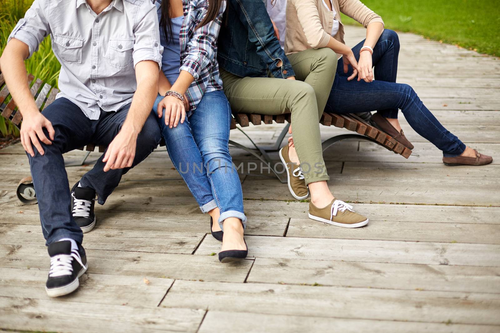 friendship, leisure, summer and people concept - close up of many legs sitting on bench at park