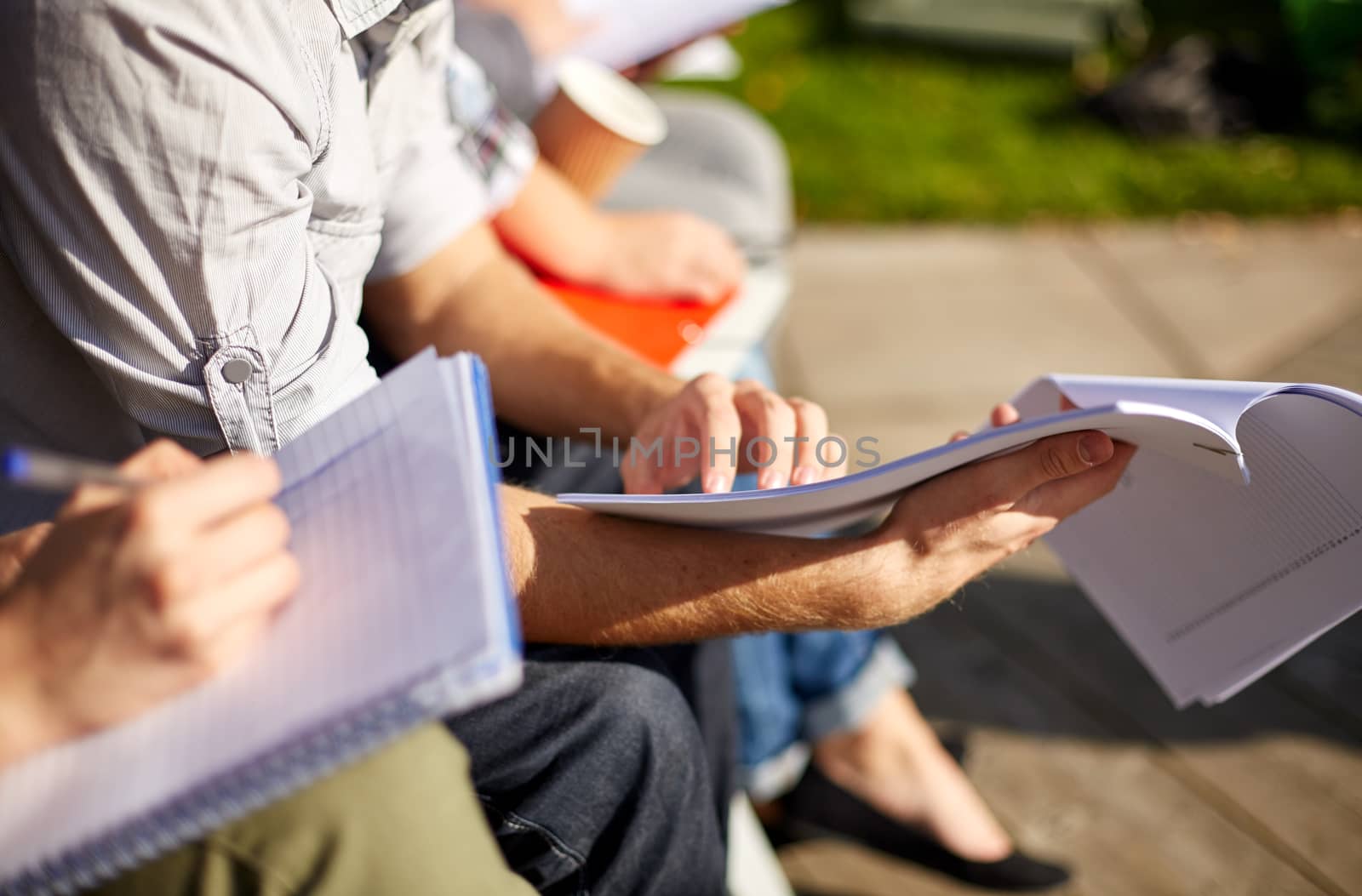 summer, friendship, education and teenage concept - close up of students with notebooks reading and writing at campus