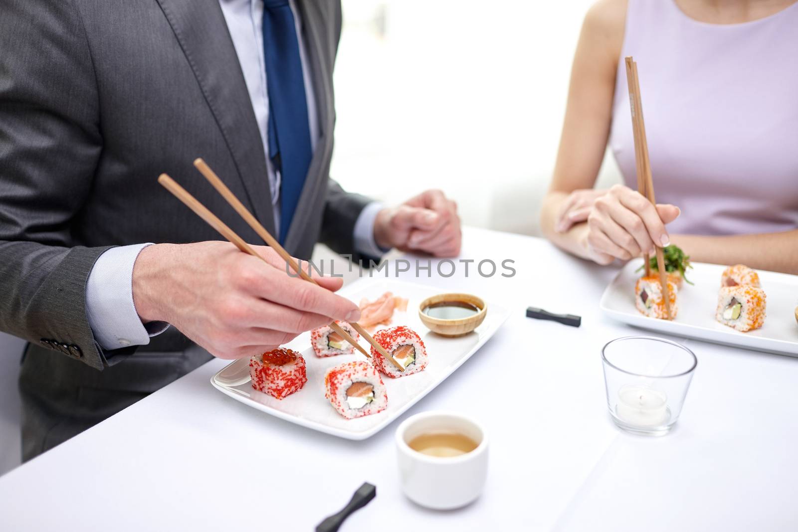 close up of couple eating sushi at restaurant by dolgachov