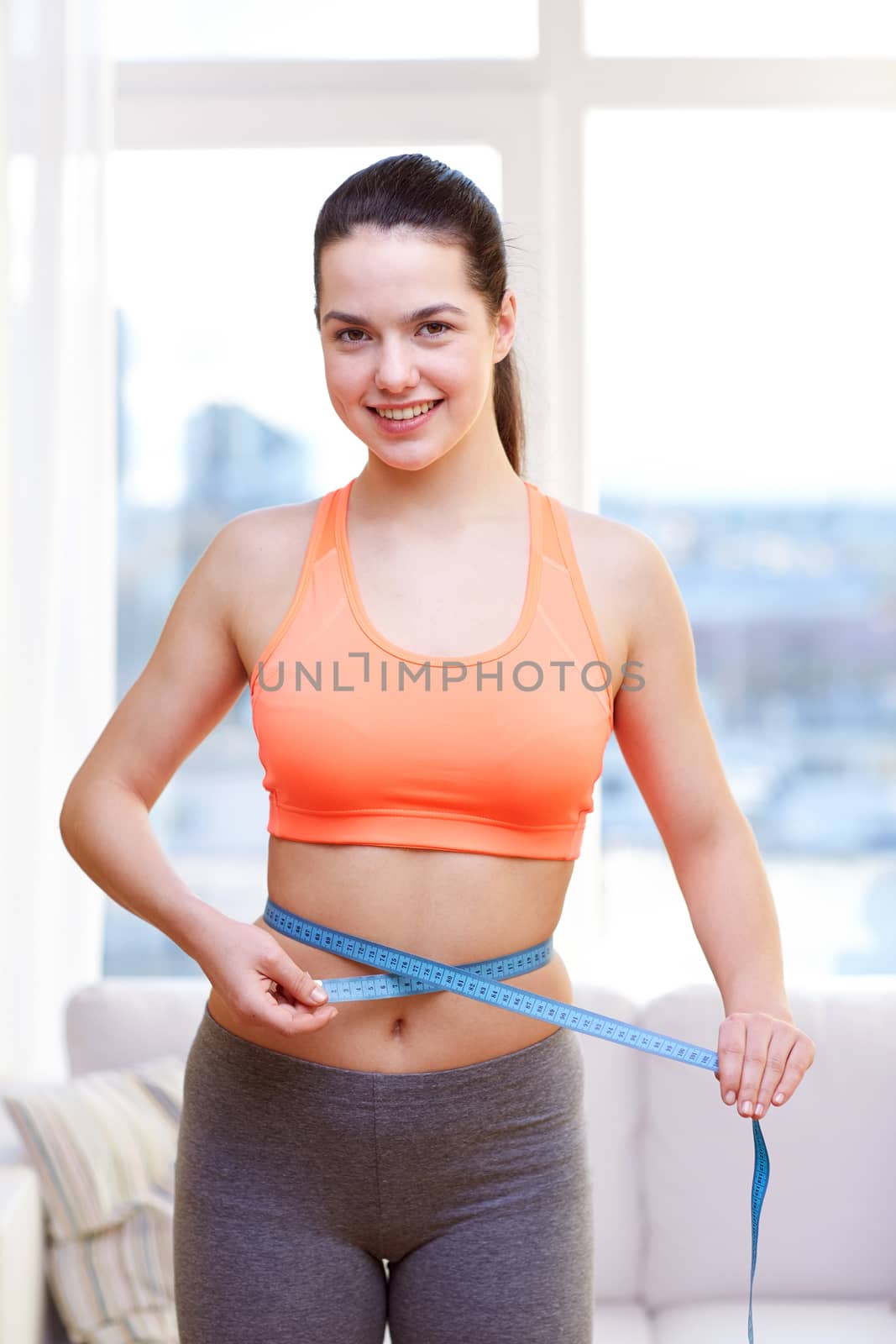 diet, slimming, sport, healthy lifestyle and people concept - happy sporty woman measuring her waist with tape at home