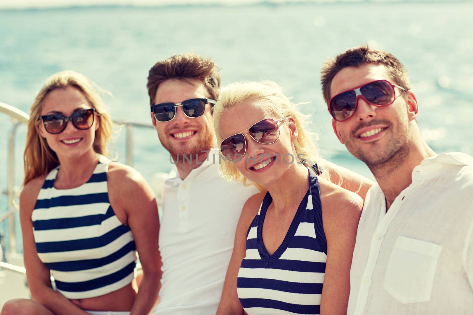 smiling friends sitting on yacht deck by dolgachov