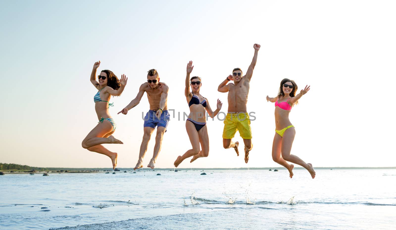 friendship, sea, summer vacation, holidays and people concept - group of smiling friends wearing swimwear and sunglasses jumping on beach