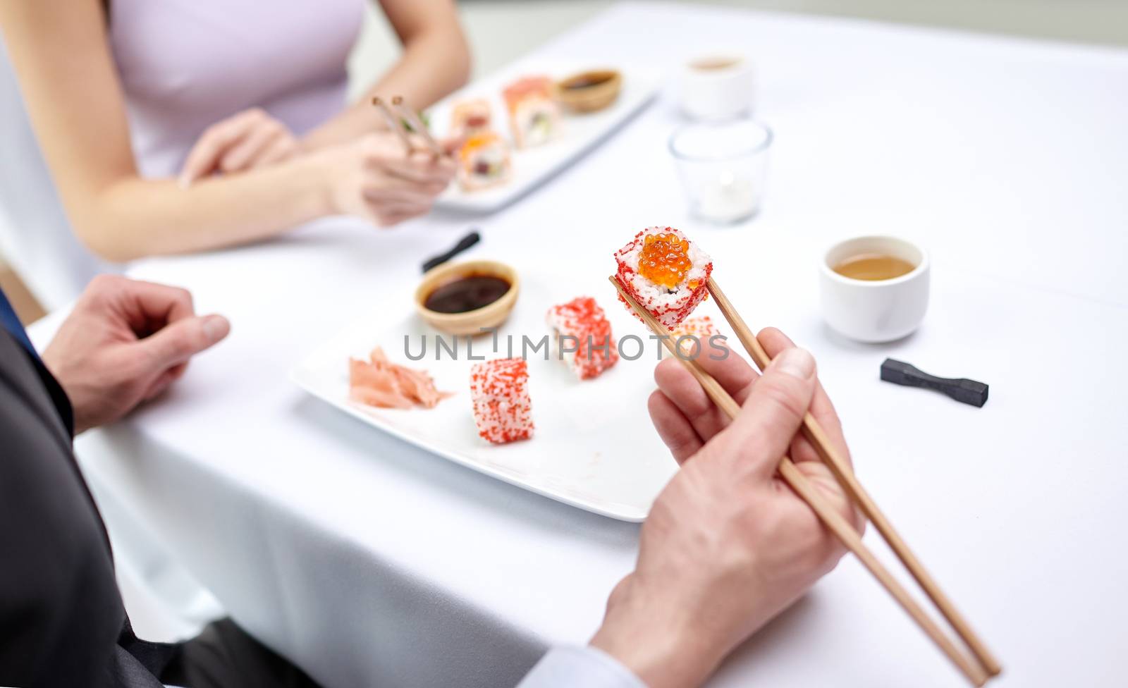 restaurant, food, people, date and holiday concept - close up of couple eating sushi at restaurant