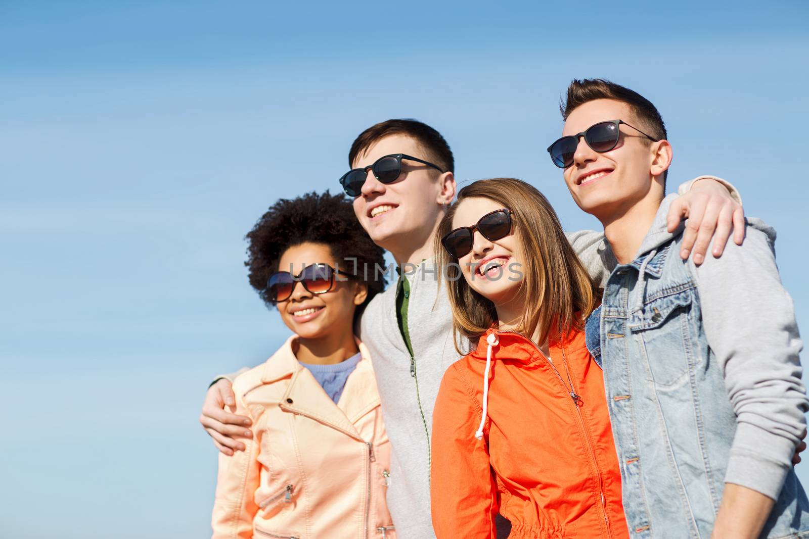 friendship, tourism, travel and people concept - group of happy teenage friends in sunglasses hugging outdoors