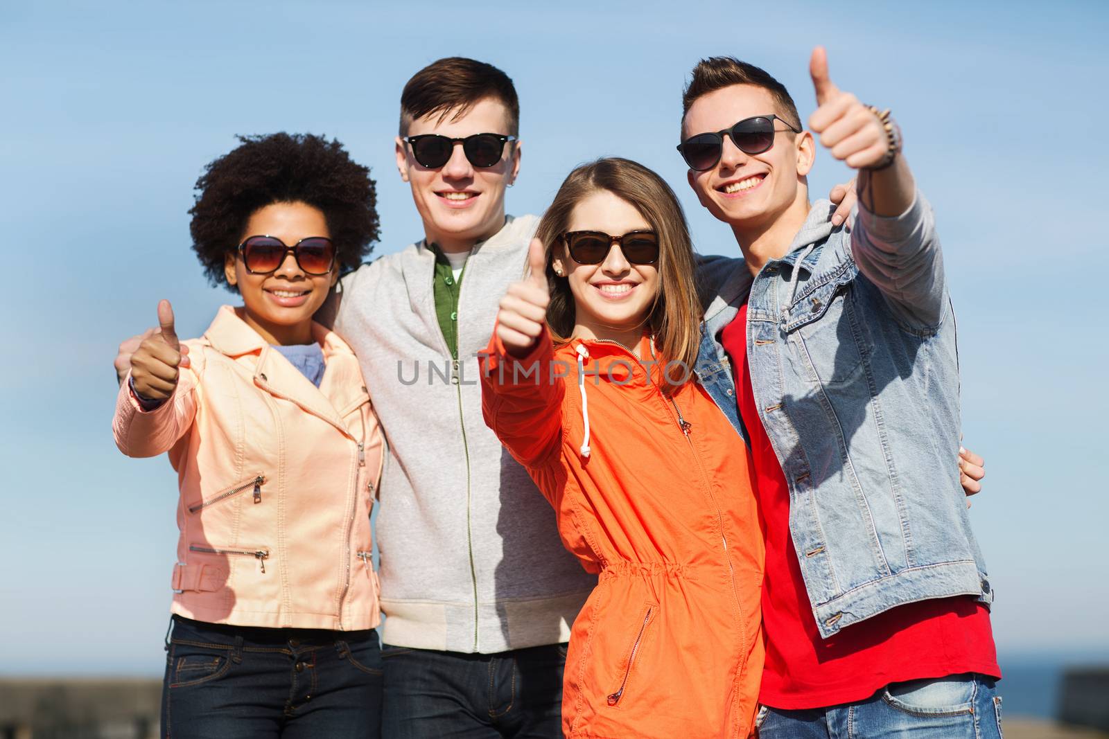 friendship, tourism, travel and people concept - group of happy teenage friends in sunglasses hugging outdoors