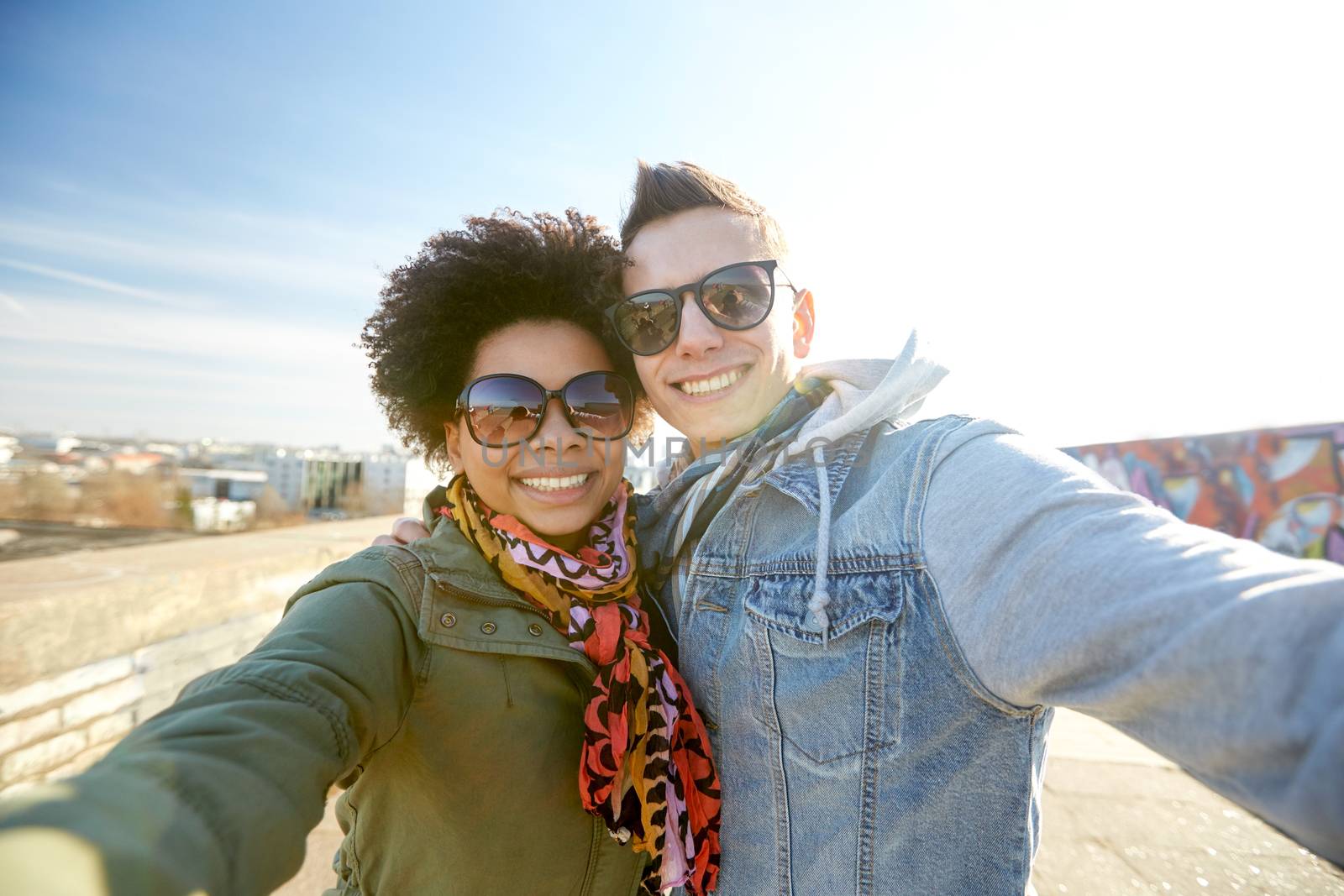 happy teenage couple taking selfie on city street by dolgachov