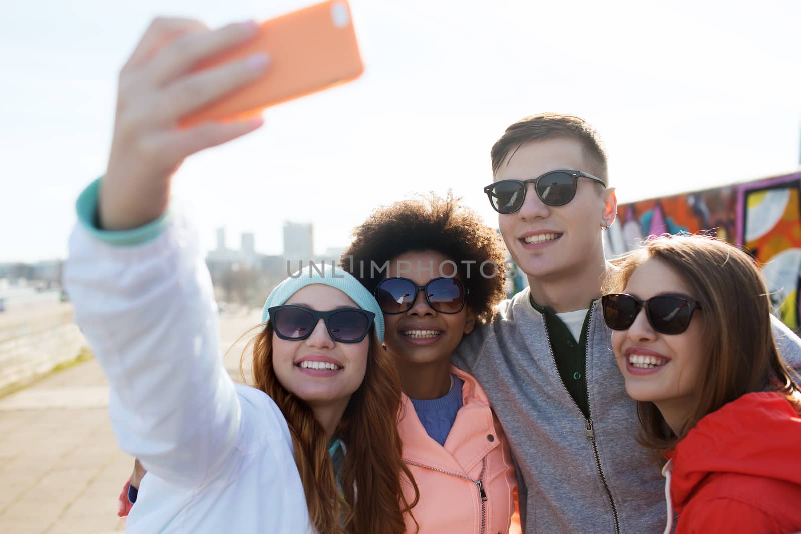 people, leisure, friendship and technology concept - group of smiling teenage friends taking selfie with smartphone outdoors