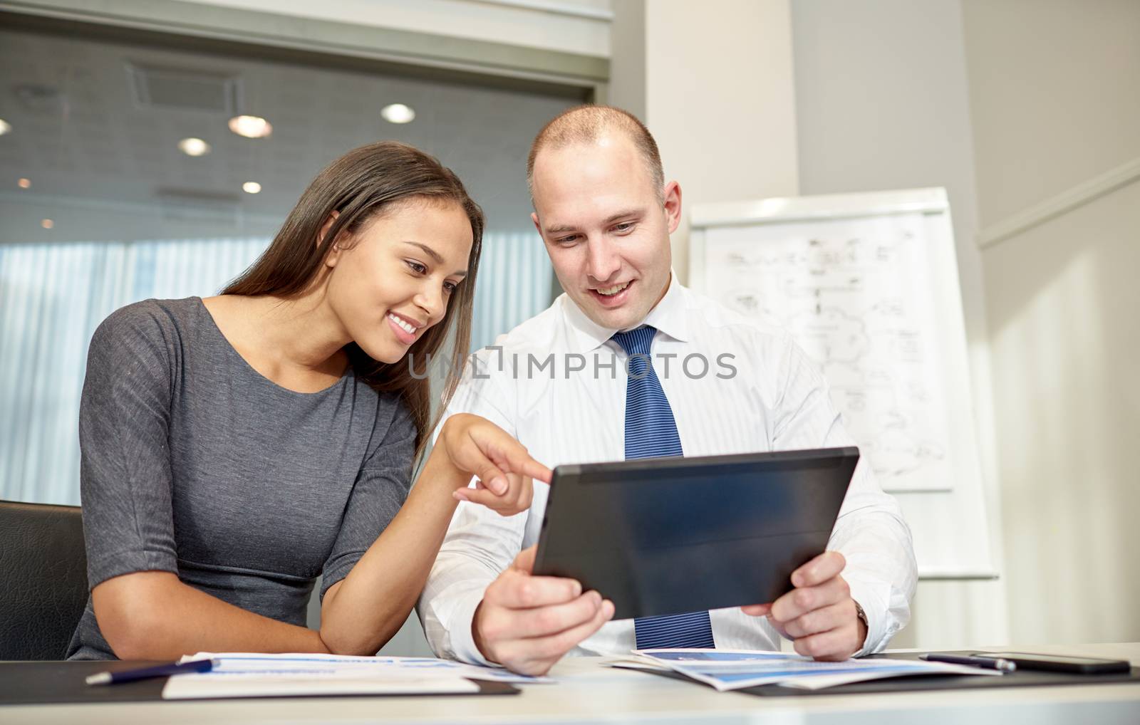 smiling businesspeople with tablet pc in office by dolgachov