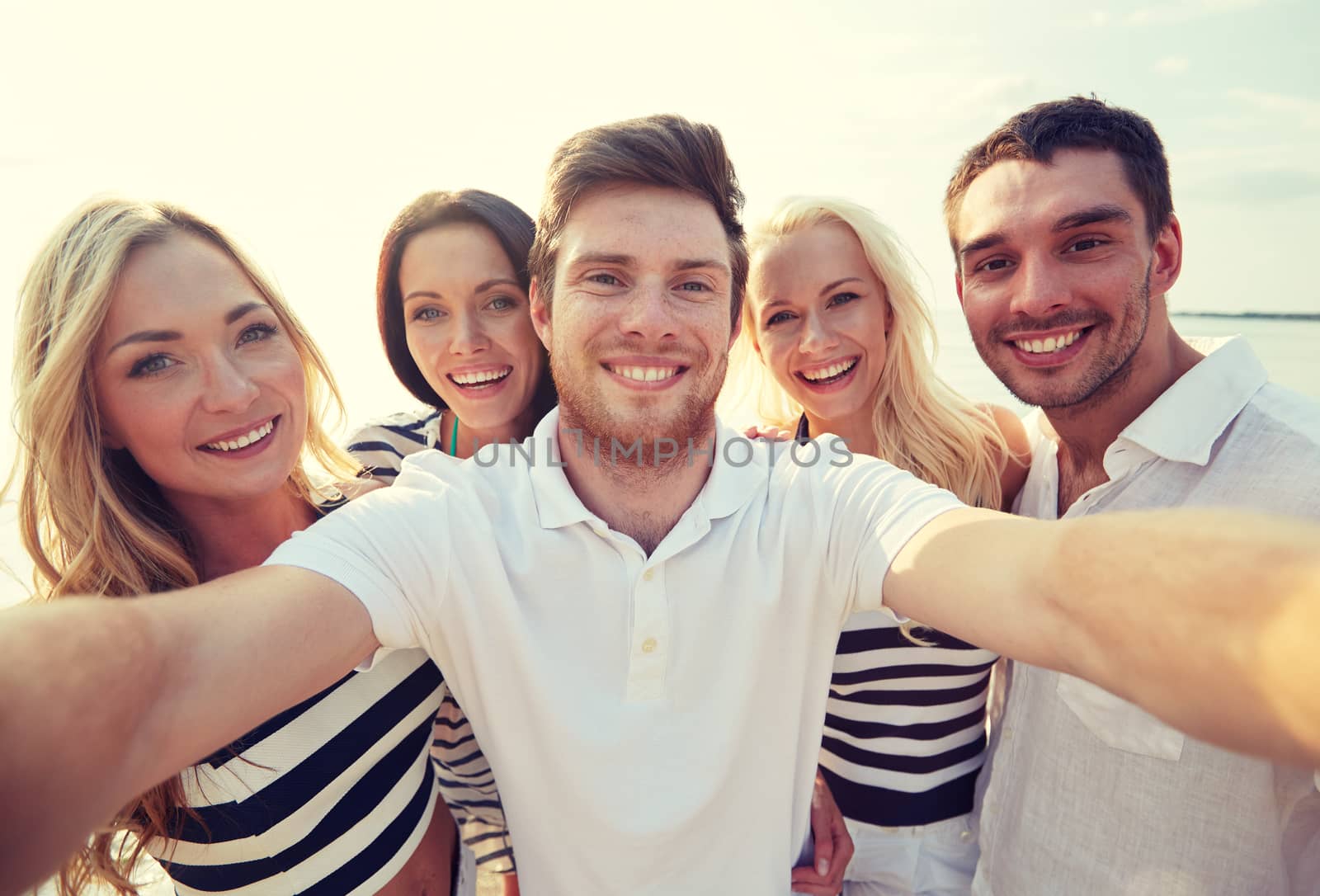 summer, sea, tourism, technology and people concept - group of smiling friends with camera on beach photographing and taking selfie